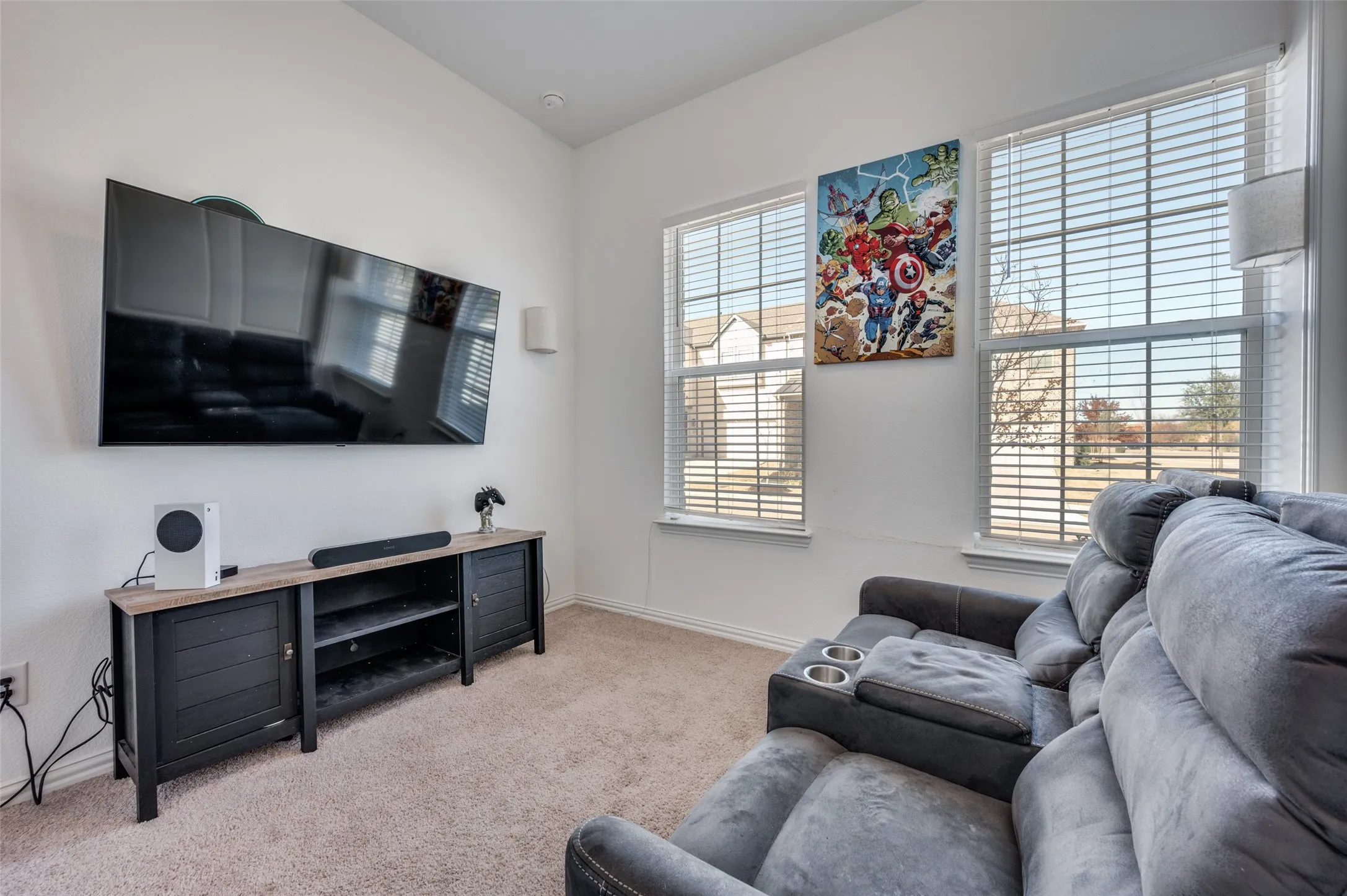 Wall-mounted display, recessed lighting, dual windows with blinds, wood-finish media console, and carpeted flooring