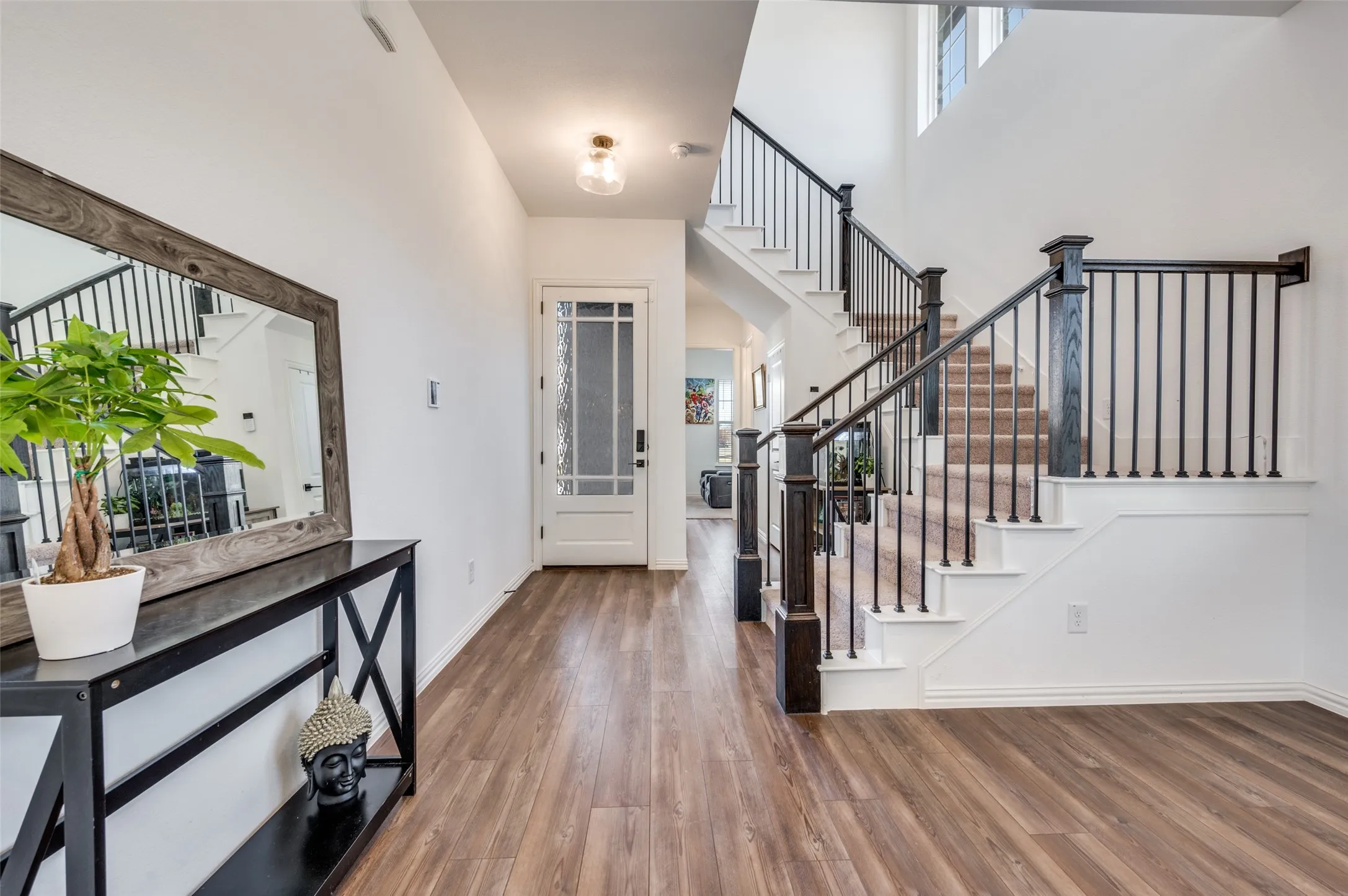 Entryway featuring wood-finish flooring, a white paneled door with decorative glass, and a staircase with dark wood newel posts and metal balusters