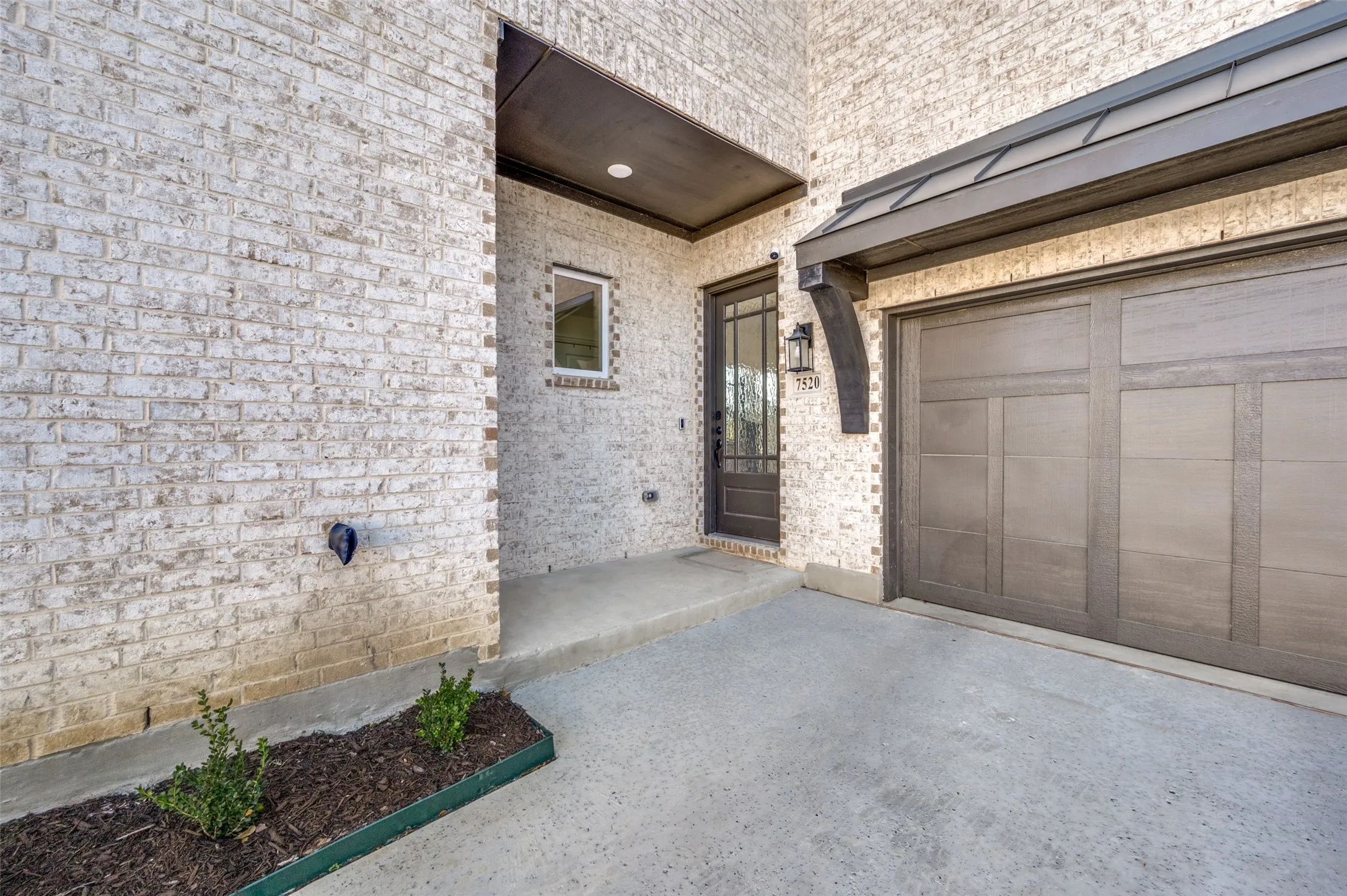 White brick exterior with dark trim accents, featuring a paneled garage door and a covered entryway with a full-light door