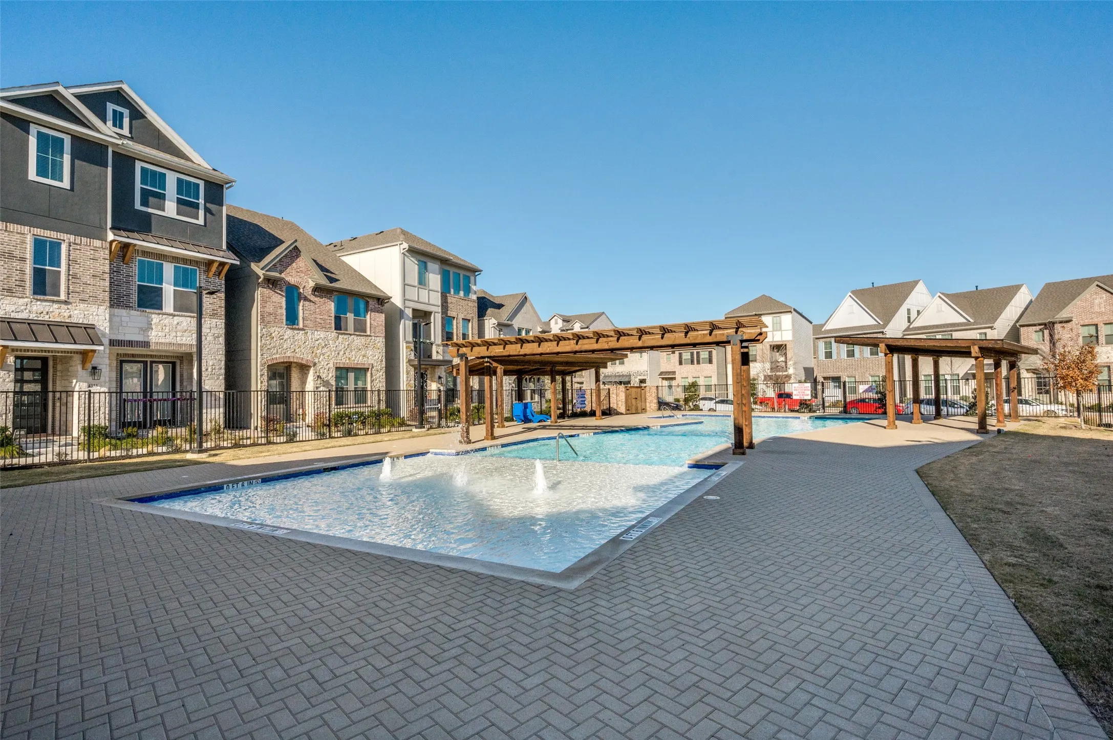 Swimming pool with water features, surrounded by a paver deck and two wood pergolas