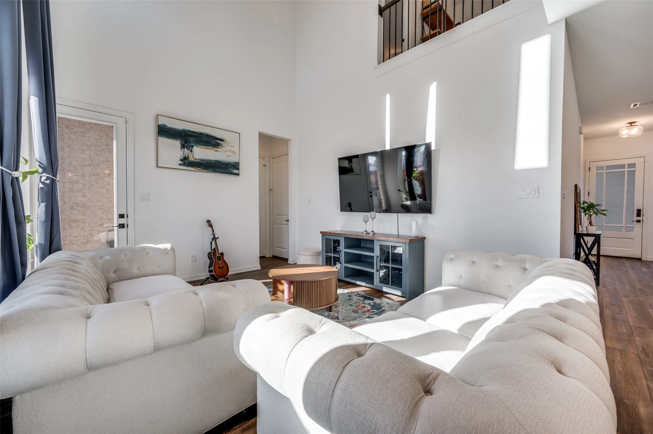 Two-story interior with wood-finish flooring, a media console, and an upper-level balcony with metal railing