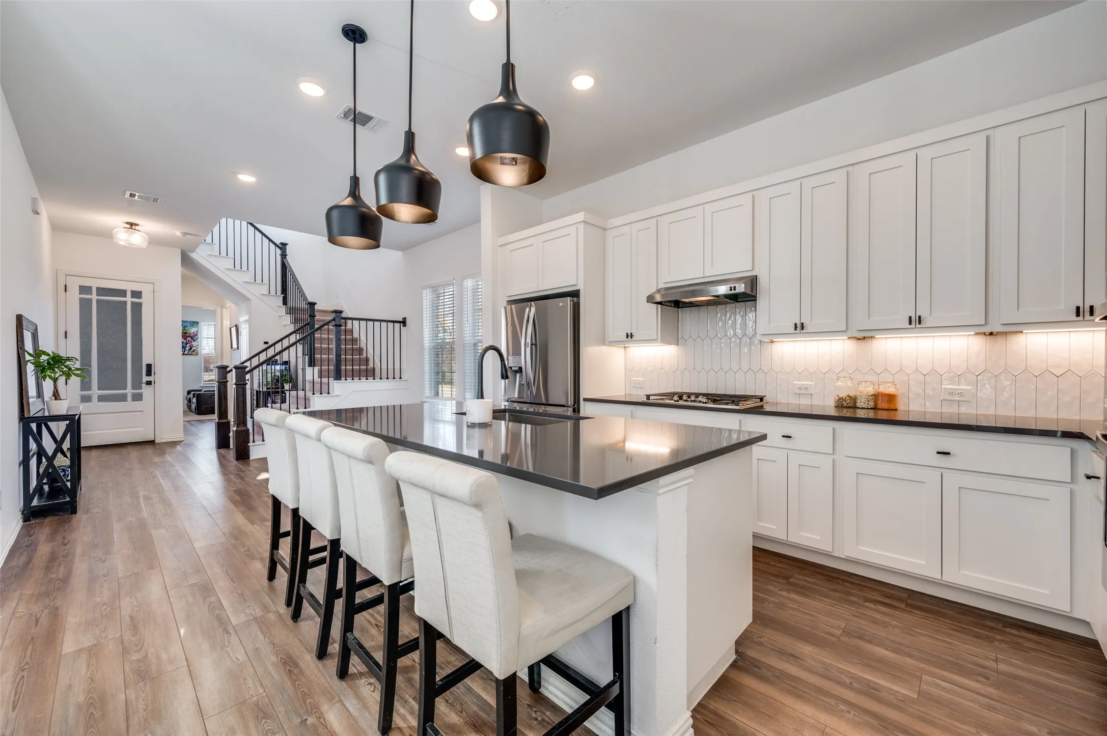Kitchen featuring a large island with dark countertops, white cabinetry with dark hardware, and a tile backsplash