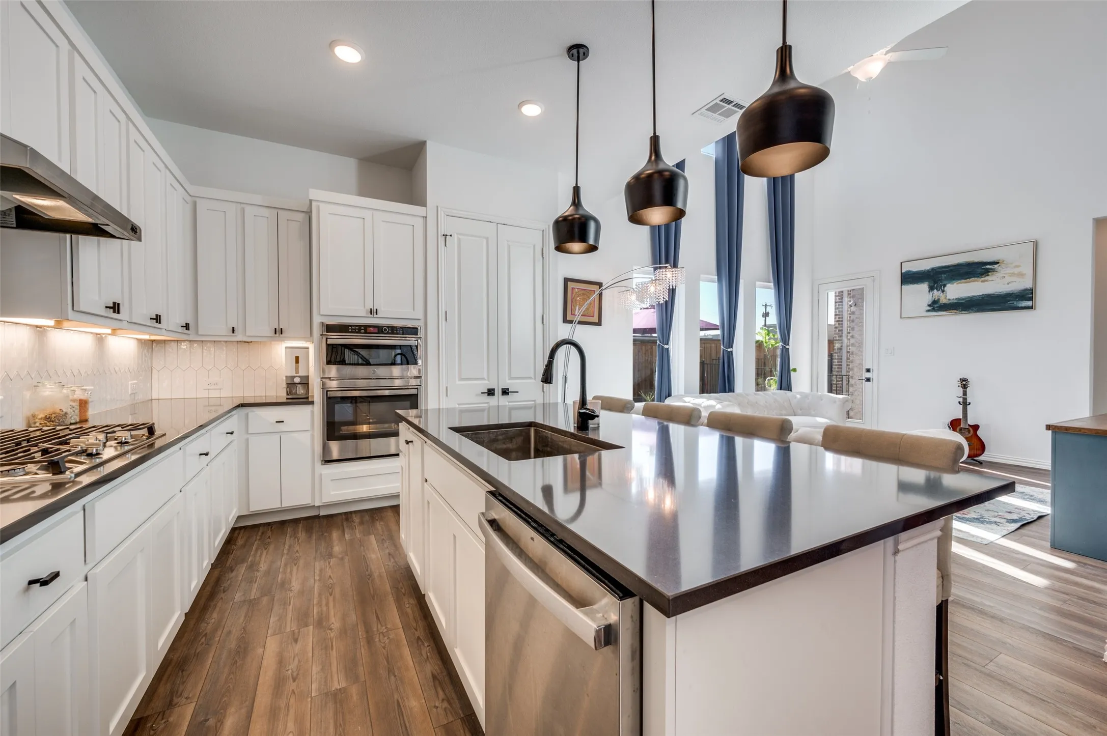 Chef's kitchen featuring white shaker cabinetry, stainless steel appliances including a dual oven configuration, and a large waterfall-edge island with a dark countertop