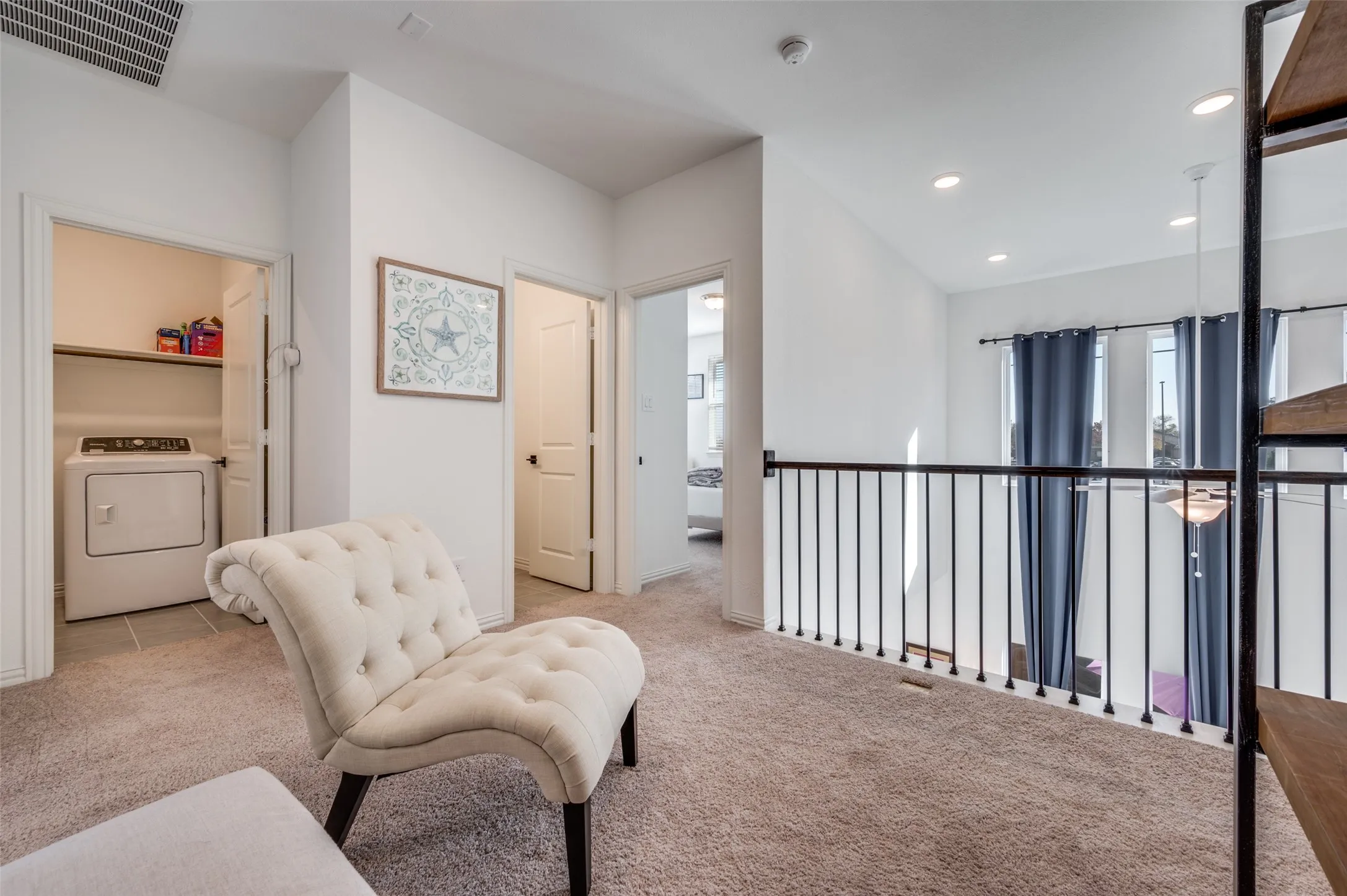 Open loft area with neutral carpet flooring and a black metal railing