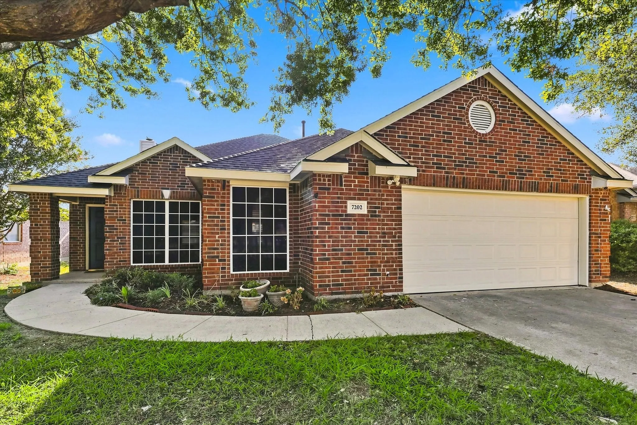 Brick exterior with a covered entry, attached garage, and a curved concrete walkway