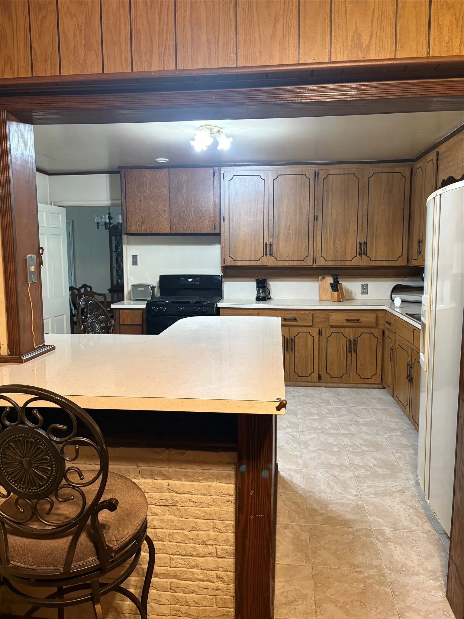 Kitchen featuring wood-finish cabinetry, white countertops, black appliances, and light-toned flooring