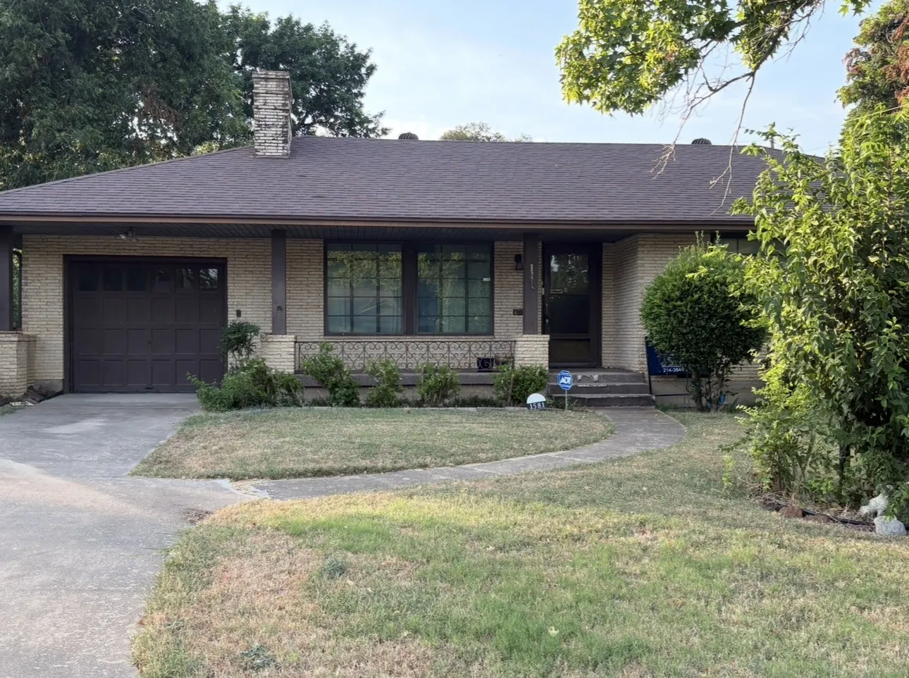 Exterior featuring light brick facade, dark brown garage door, arched concrete pathway, and a decorative wrought iron railing