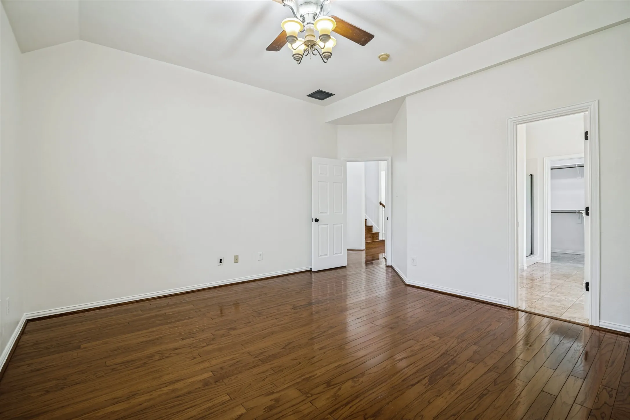 Hardwood flooring throughout, vaulted ceiling, ceiling fan with integrated lighting, white interior doors, and neutral wall tones