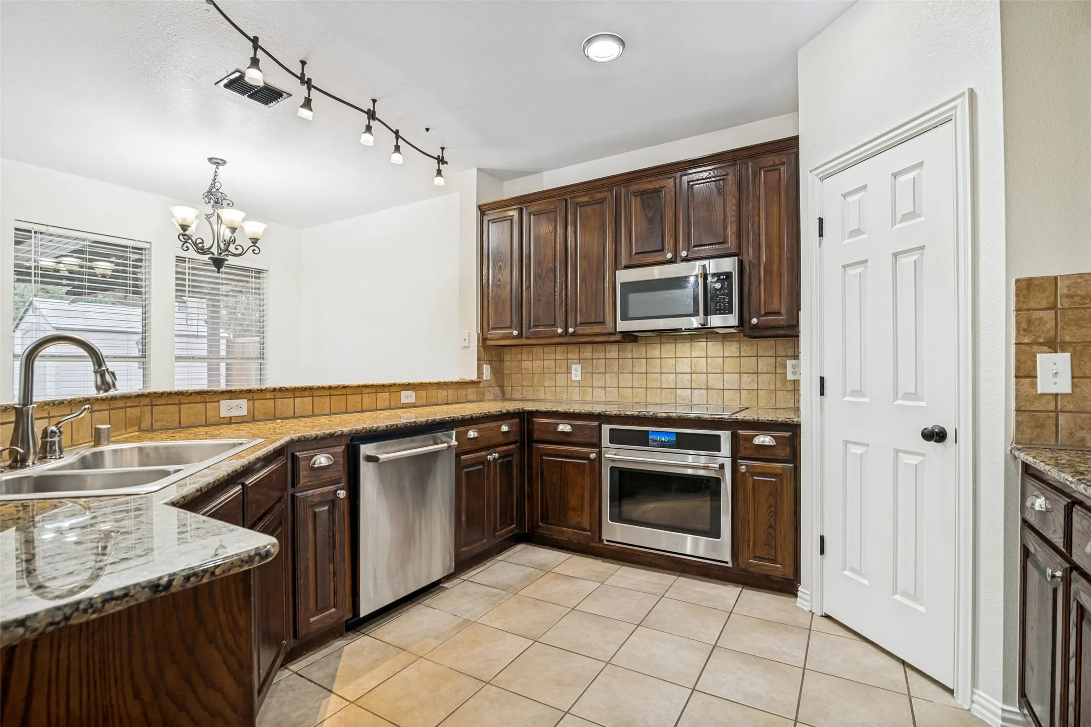 Kitchen featuring stainless steel appliances, wood cabinetry, extra tall custom upper cabinets, tile flooring, granite countertops, and a tile backsplash