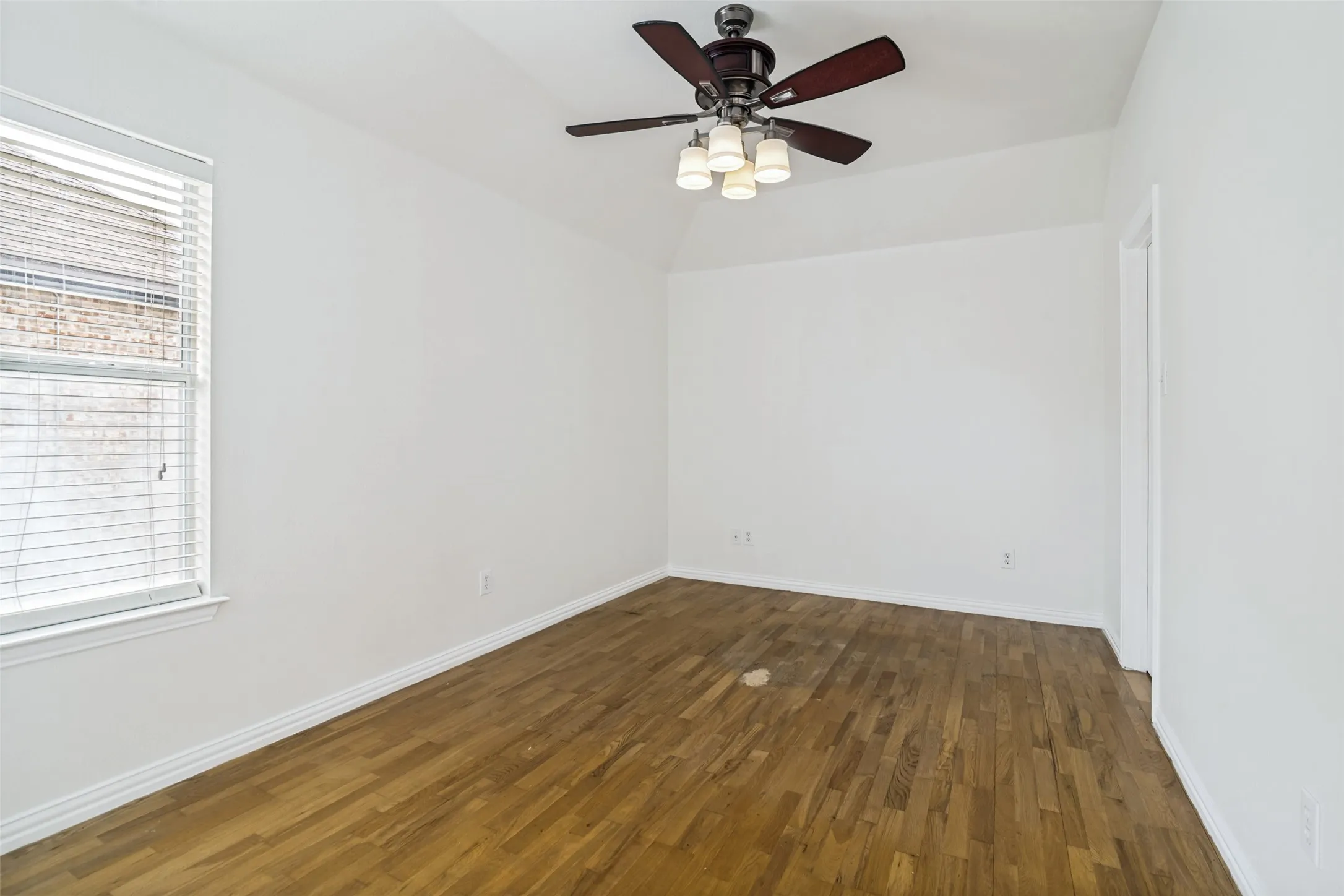 Spacious room featuring wood-finish flooring, a tray ceiling, and a ceiling fan with integrated lighting