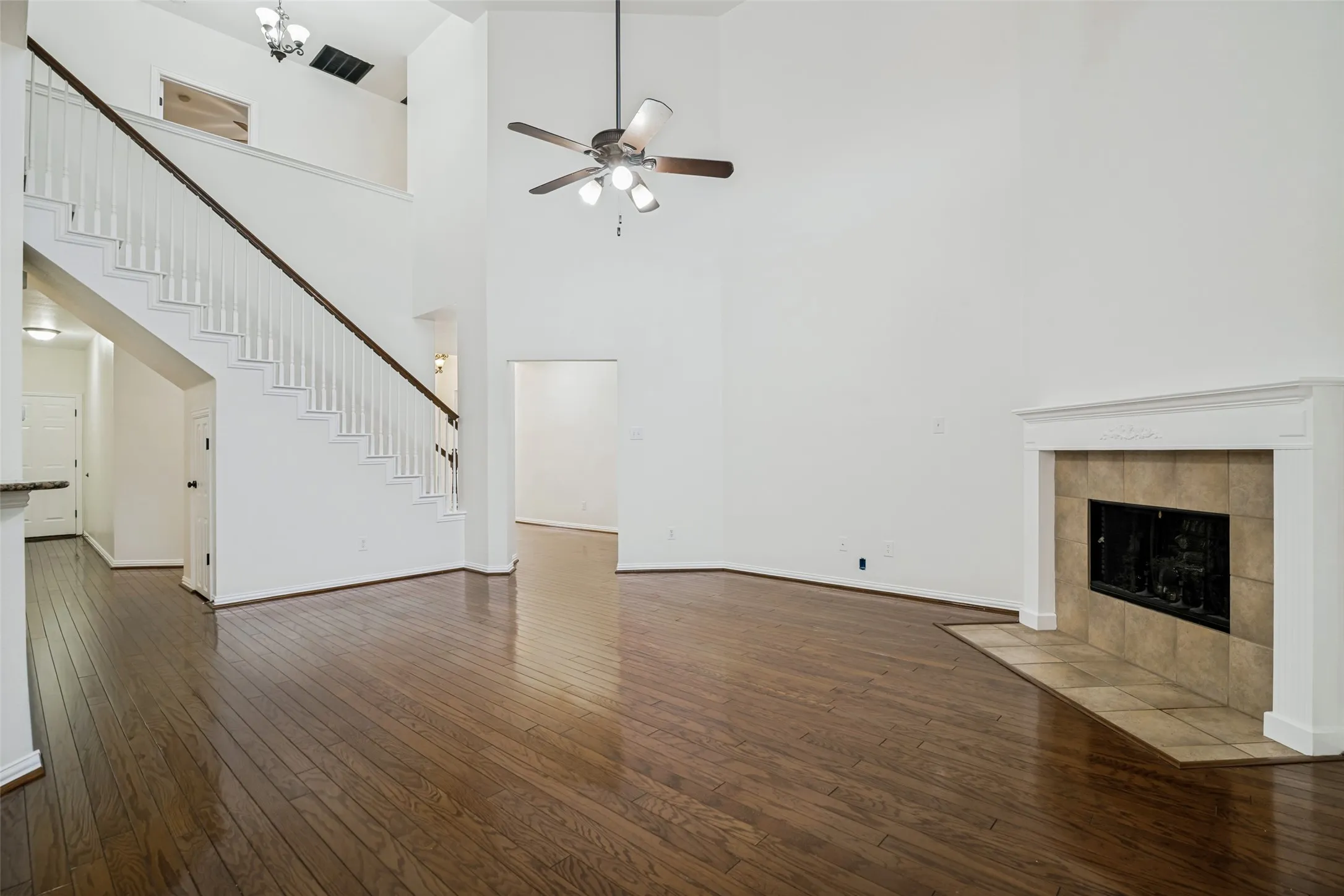 Vaulted ceilings, wood-finish flooring, a decorative fireplace with tile surround, a ceiling fan, and a staircase with a white balustrade