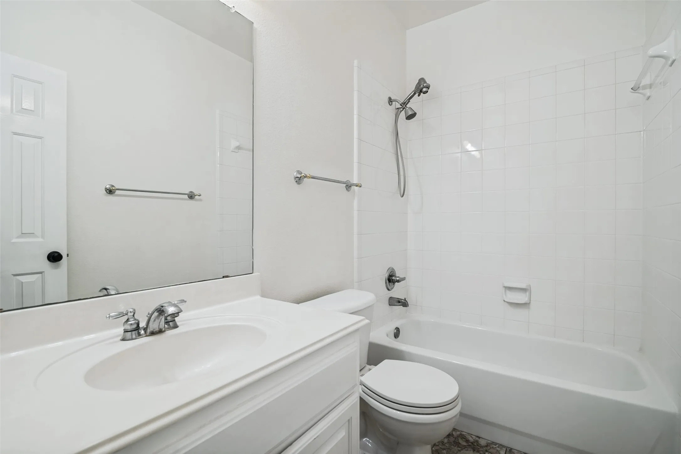 Black and white patterned tile flooring, white vanity with integrated sink, chrome faucet, full-width vanity mirror, and white tiled shower/tub combination