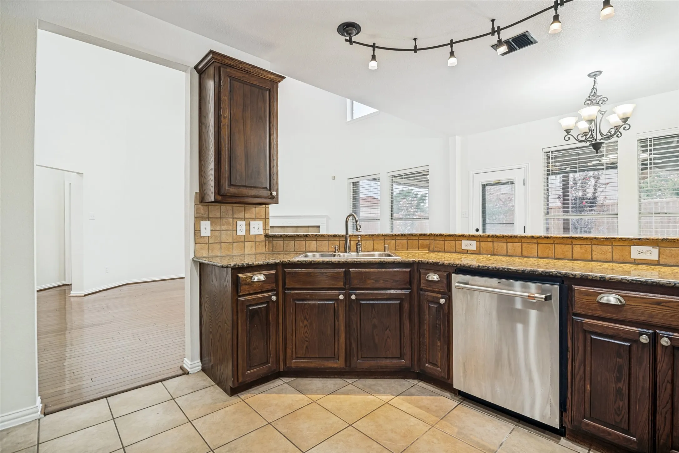 Kitchen featuring wood cabinetry, an integrated sink, stainless steel dishwasher, track lighting, and tile flooring
