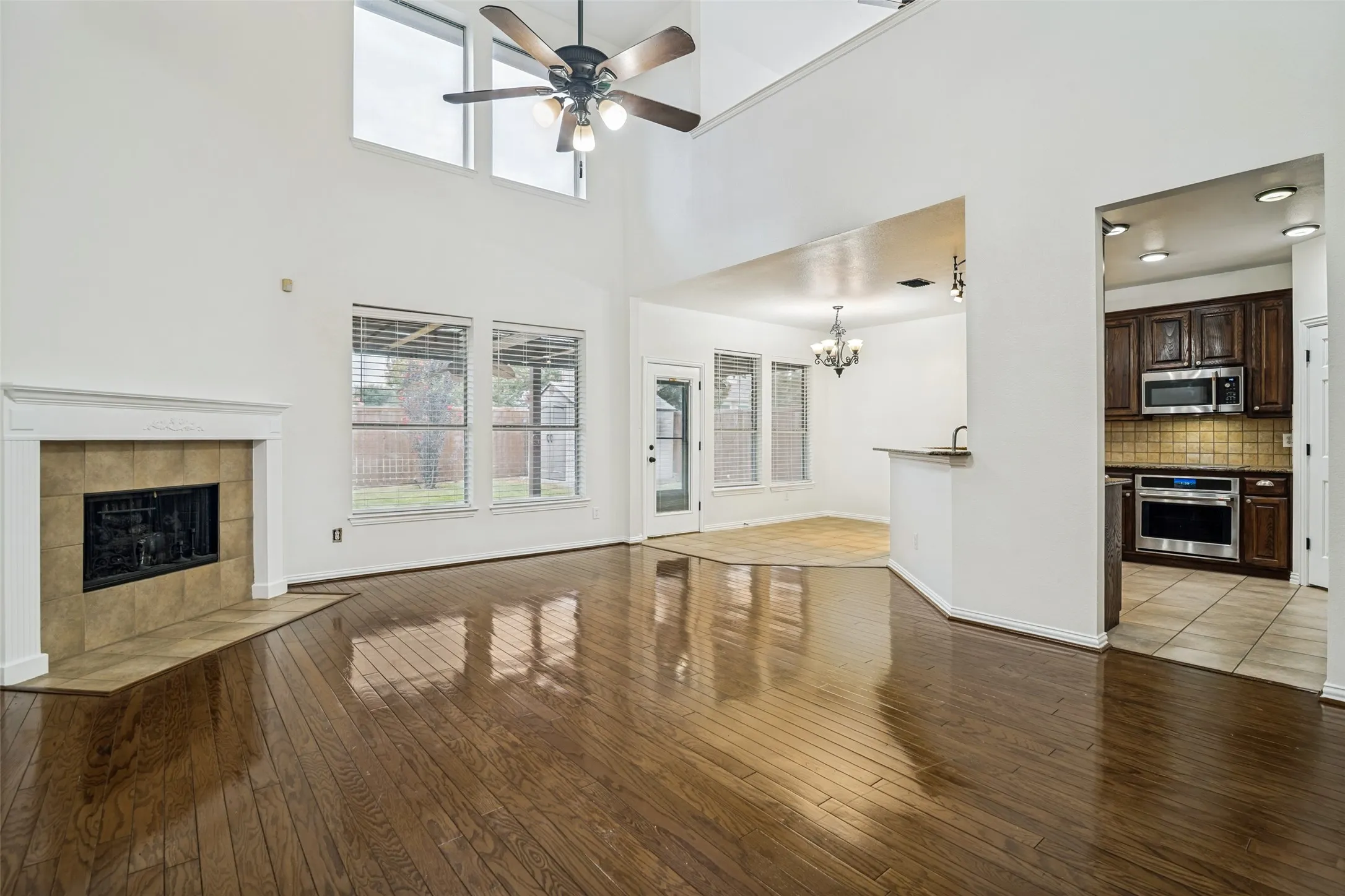 Vaulted ceilings with an upper window, wood-finish flooring, a fireplace with a tile surround, and a kitchen featuring stainless steel appliances and wood cabinetry, tall custom upper cabinets in kitchen.