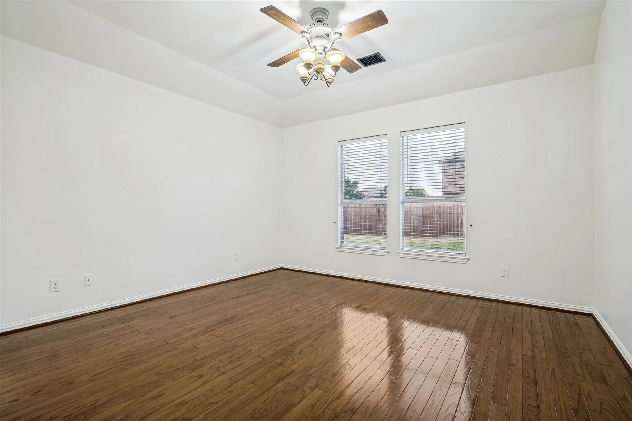 Tray ceiling with a decorative ceiling fan, two windows with blinds, and wood-finish flooring