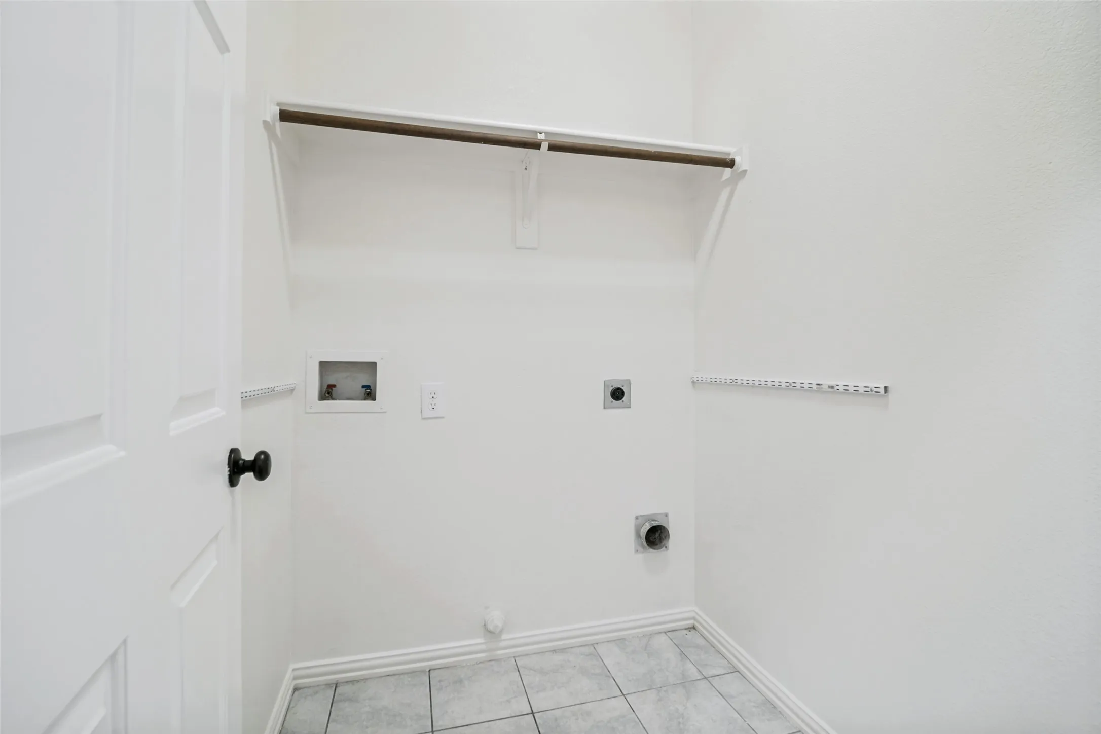 White paneled door with black hardware, tile flooring, laundry connections, and built-in shelving