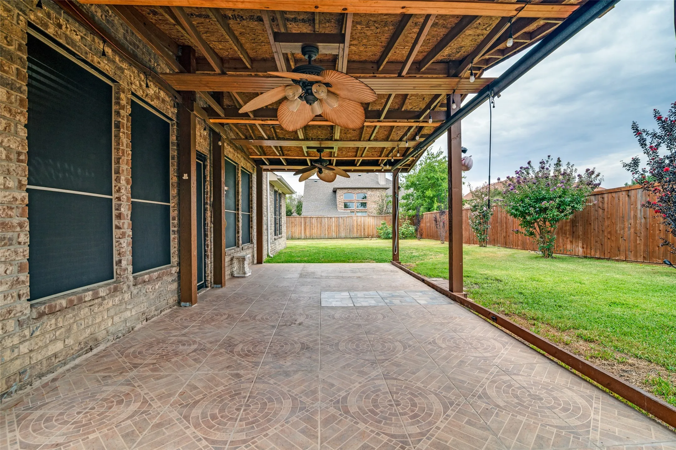 Covered patio with patterned tile flooring, exposed wood beam ceiling, and two ceiling fans