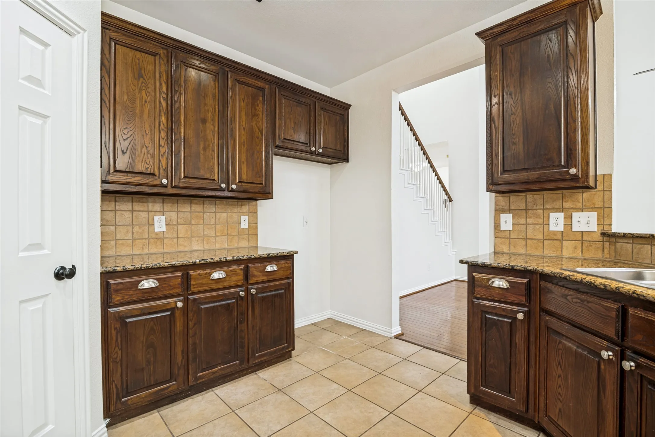 Rich wood cabinetry, including extra tall upper cabinets, with polished hardware, tile flooring, granite countertops, and a full tile backsplash