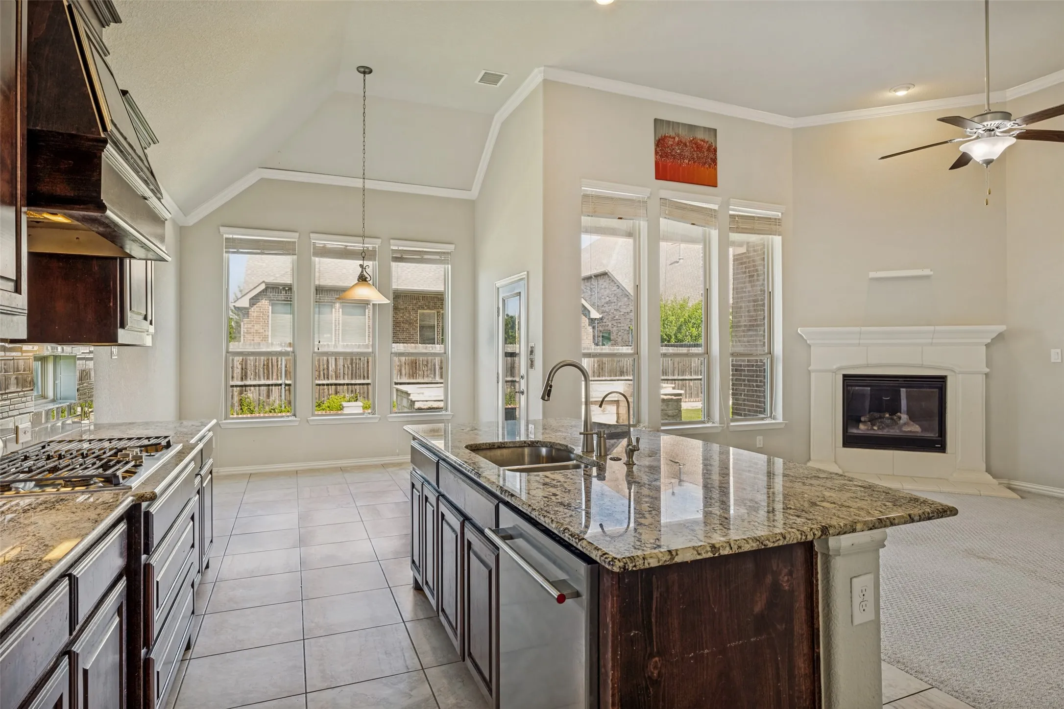 Kitchen island with an undermount sink, granite countertops, tile flooring, gas range, and a fireplace with a mantel