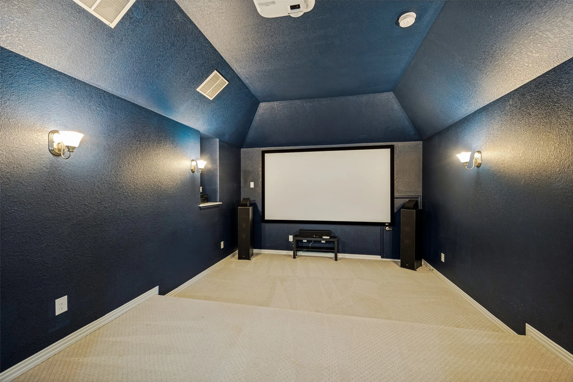 Media room with sloped ceiling, built-in projector screen, and sconce lighting