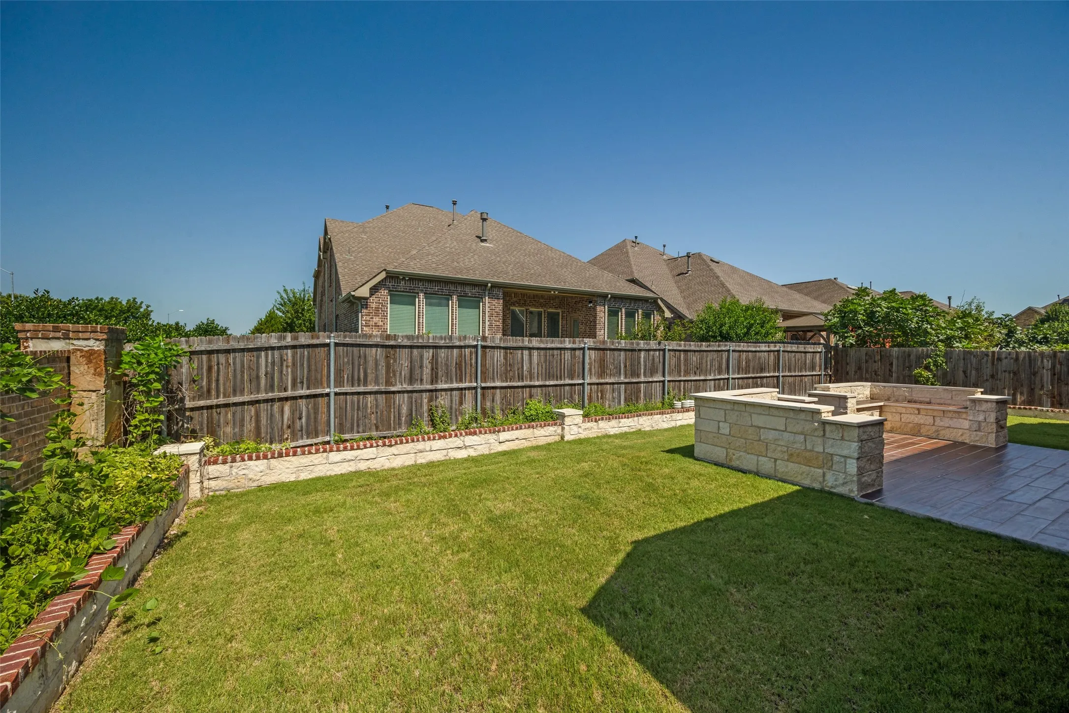 Expansive backyard featuring a stone patio, built-in stone seating, and a dedicated fire pit area
