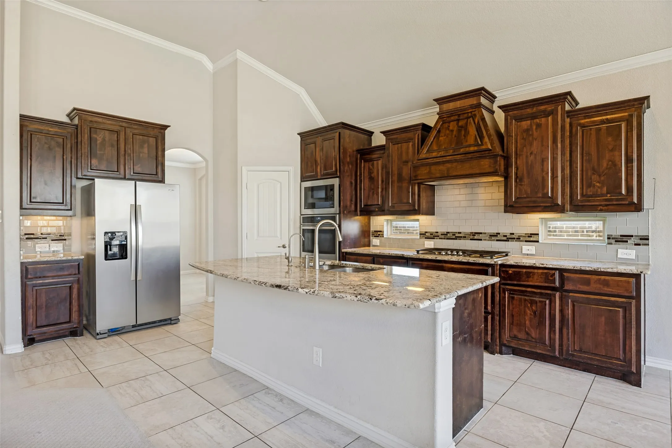 Kitchen featuring a large island with stone countertop, stainless steel appliances, wood cabinetry, subway tile backsplash, and tile flooring