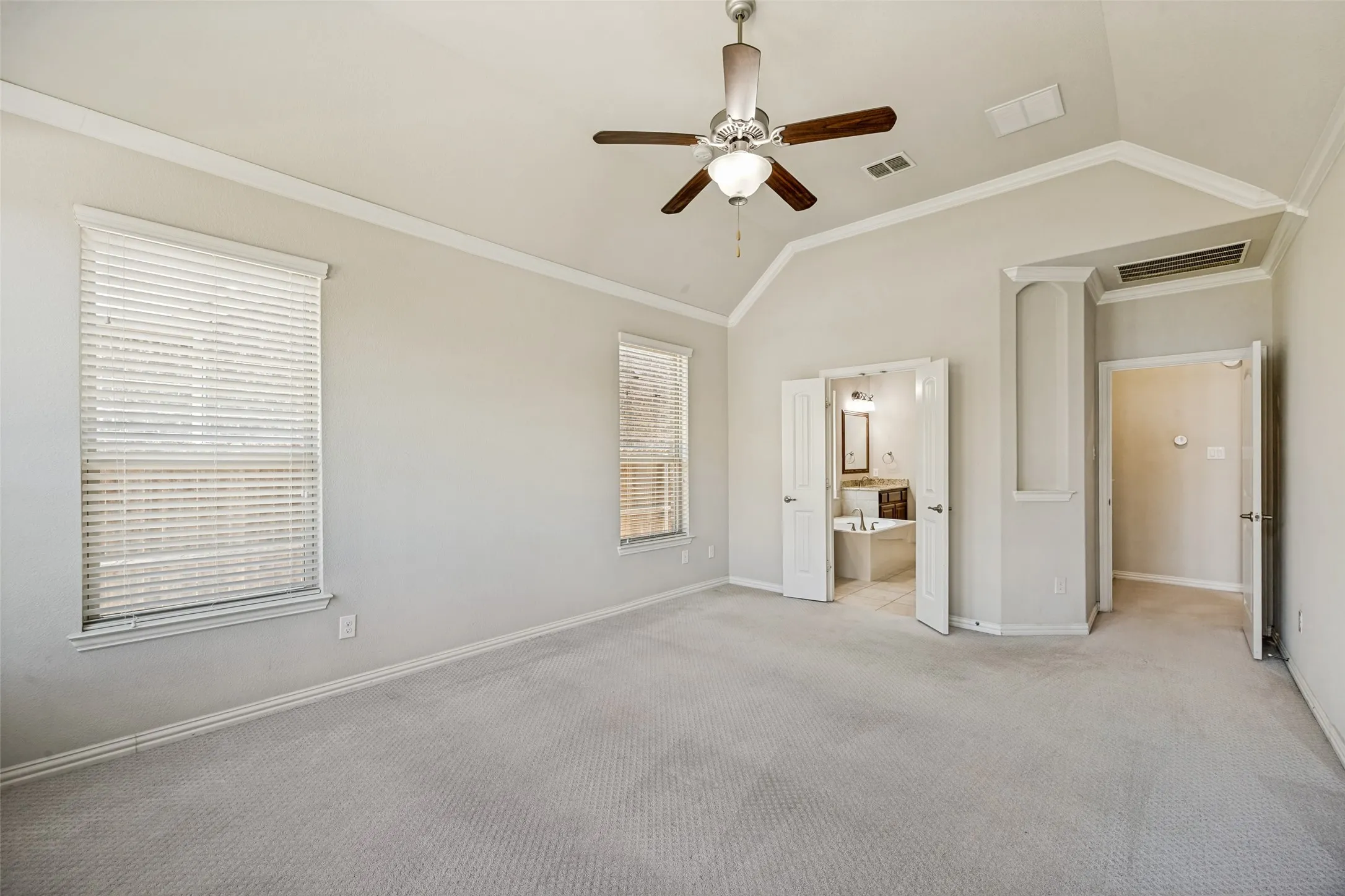 Vaulted ceiling with crown molding, two windows with blinds, a ceiling fan with light fixture, and carpeted flooring