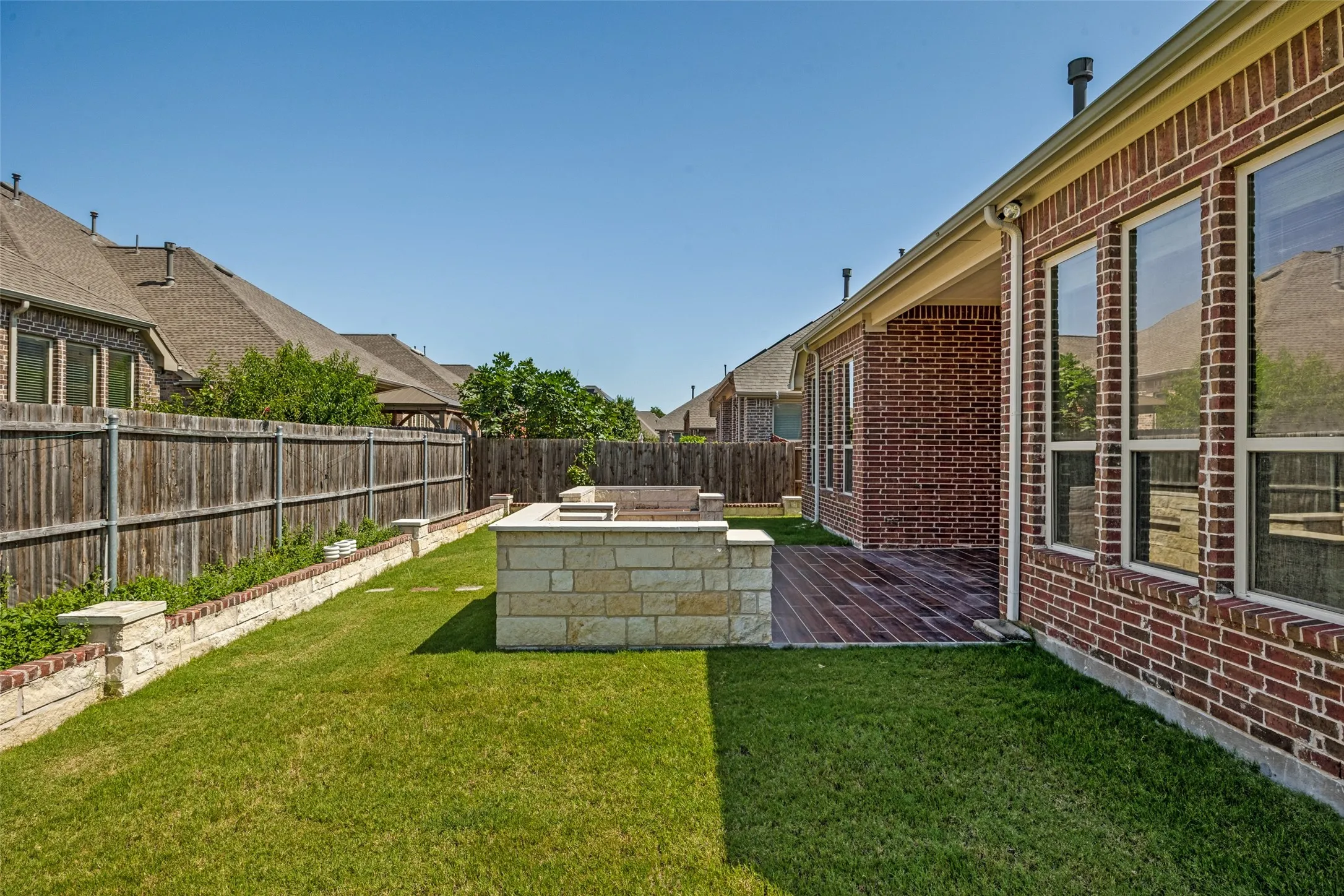 Expansive backyard featuring a manicured lawn, stone retaining wall, and a wood privacy fence