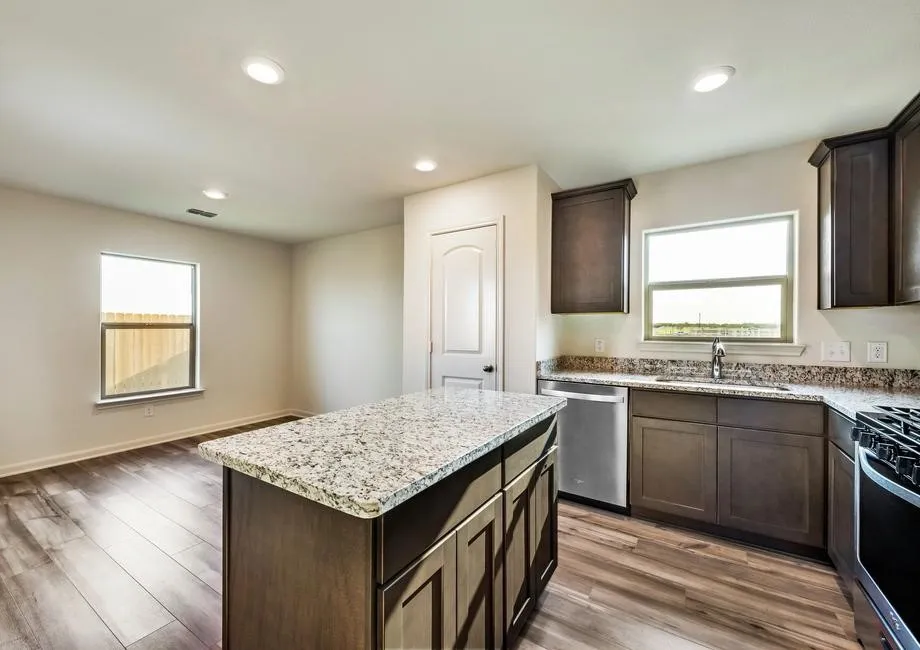 Kitchen featuring a central island with a stone-finish countertop, wood-finish flooring, dark wood-finish cabinetry, and stainless steel appliances