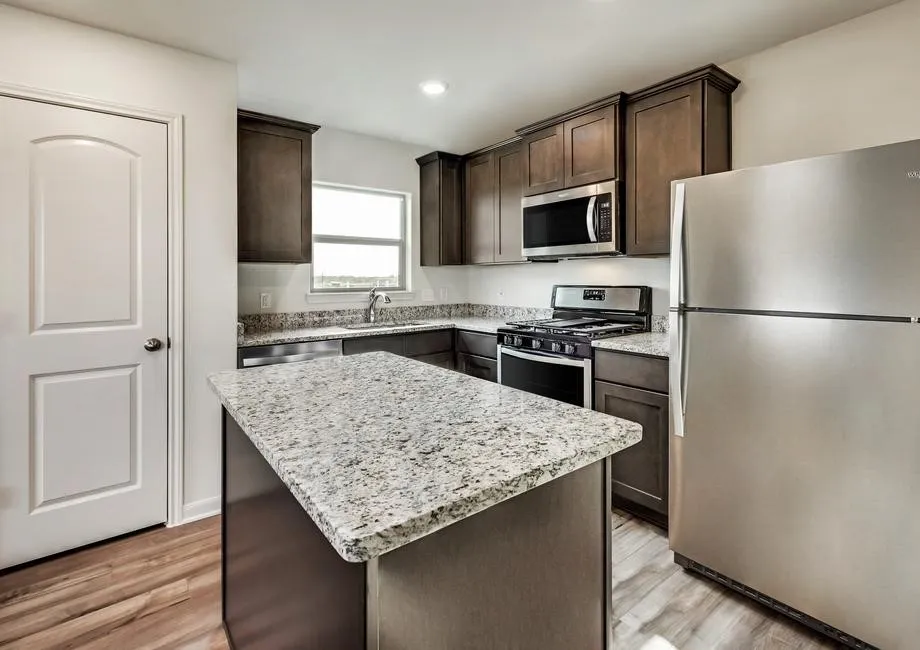 Kitchen with dark wood cabinetry, light-toned countertops, stainless steel appliances, and wood-finish flooring