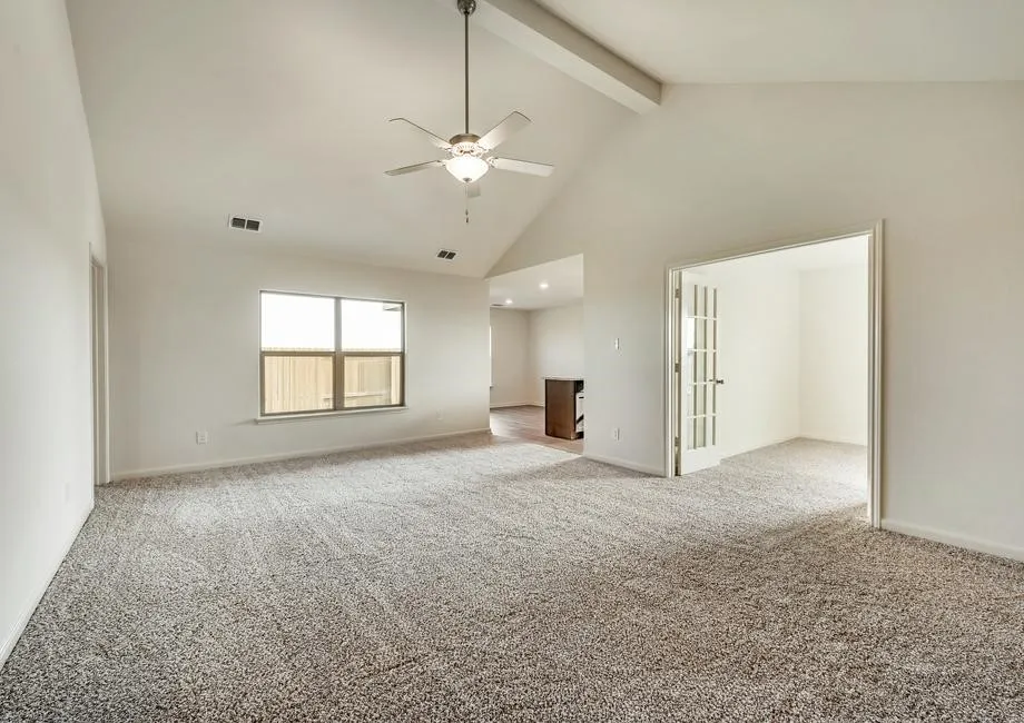 Vaulted ceiling with exposed beam, ceiling fan with light fixture, window with privacy fencing beyond, and French doors