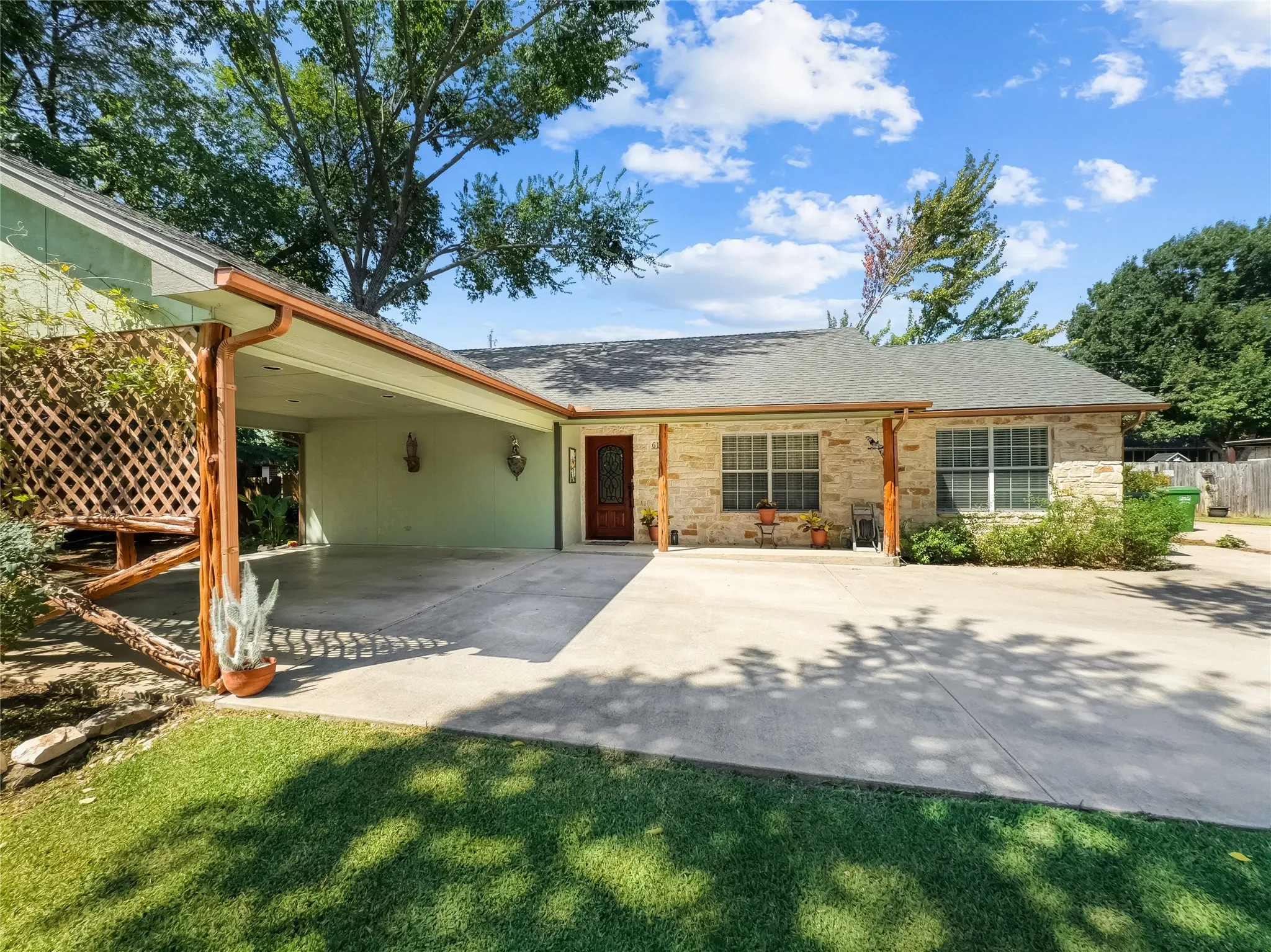 Stone facade with a covered carport, wood-finish support columns, and a lattice privacy screen