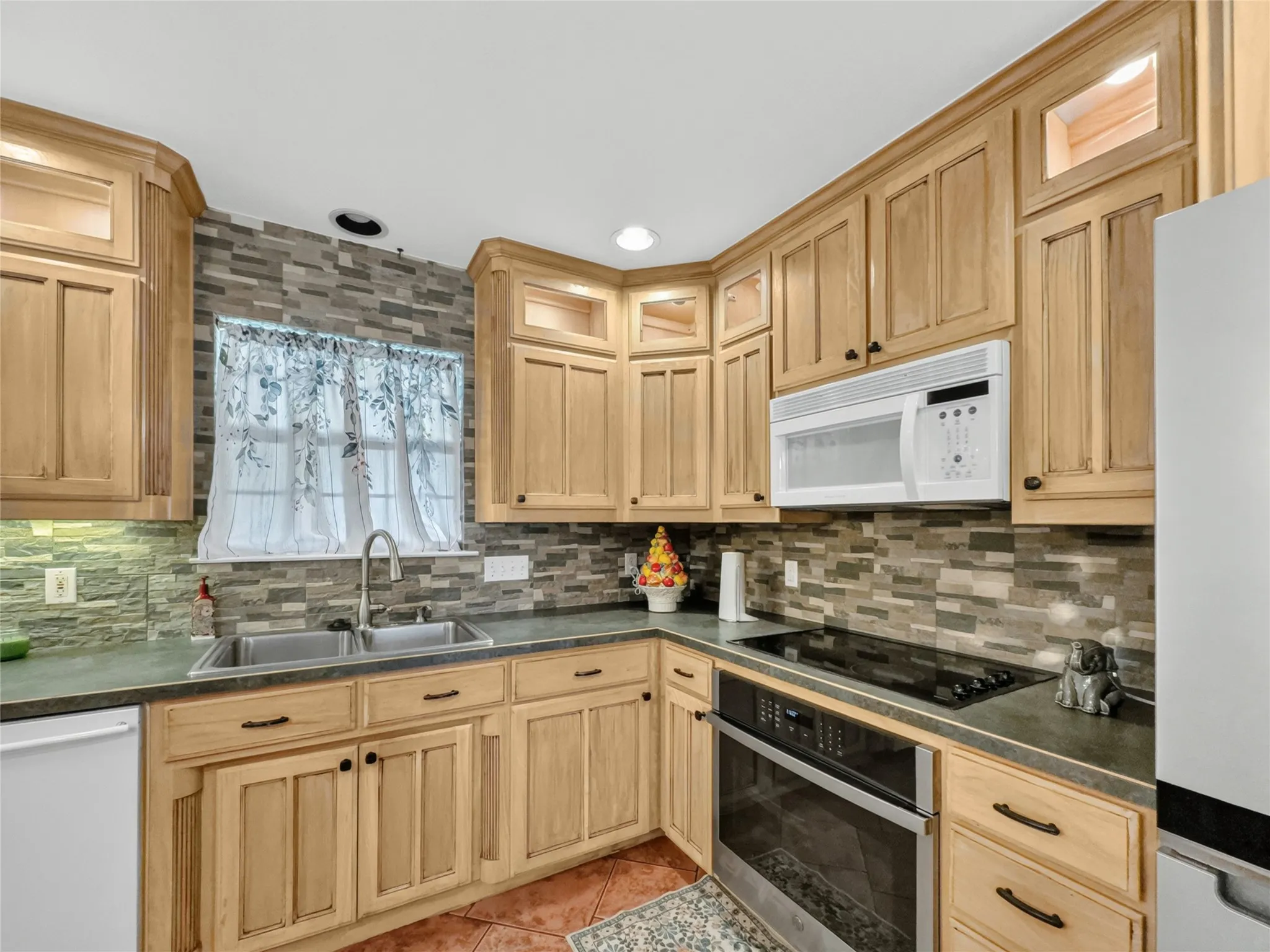 Wood-finish cabinetry with black hardware, stainless steel double-basin sink, built-in microwave, and a black cooktop with a wall oven