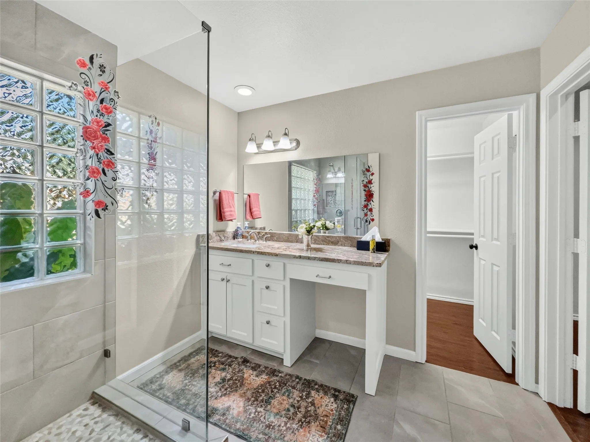 Glass-enclosed shower with pebble flooring and glass block window, double vanity with stone countertop, and tile flooring