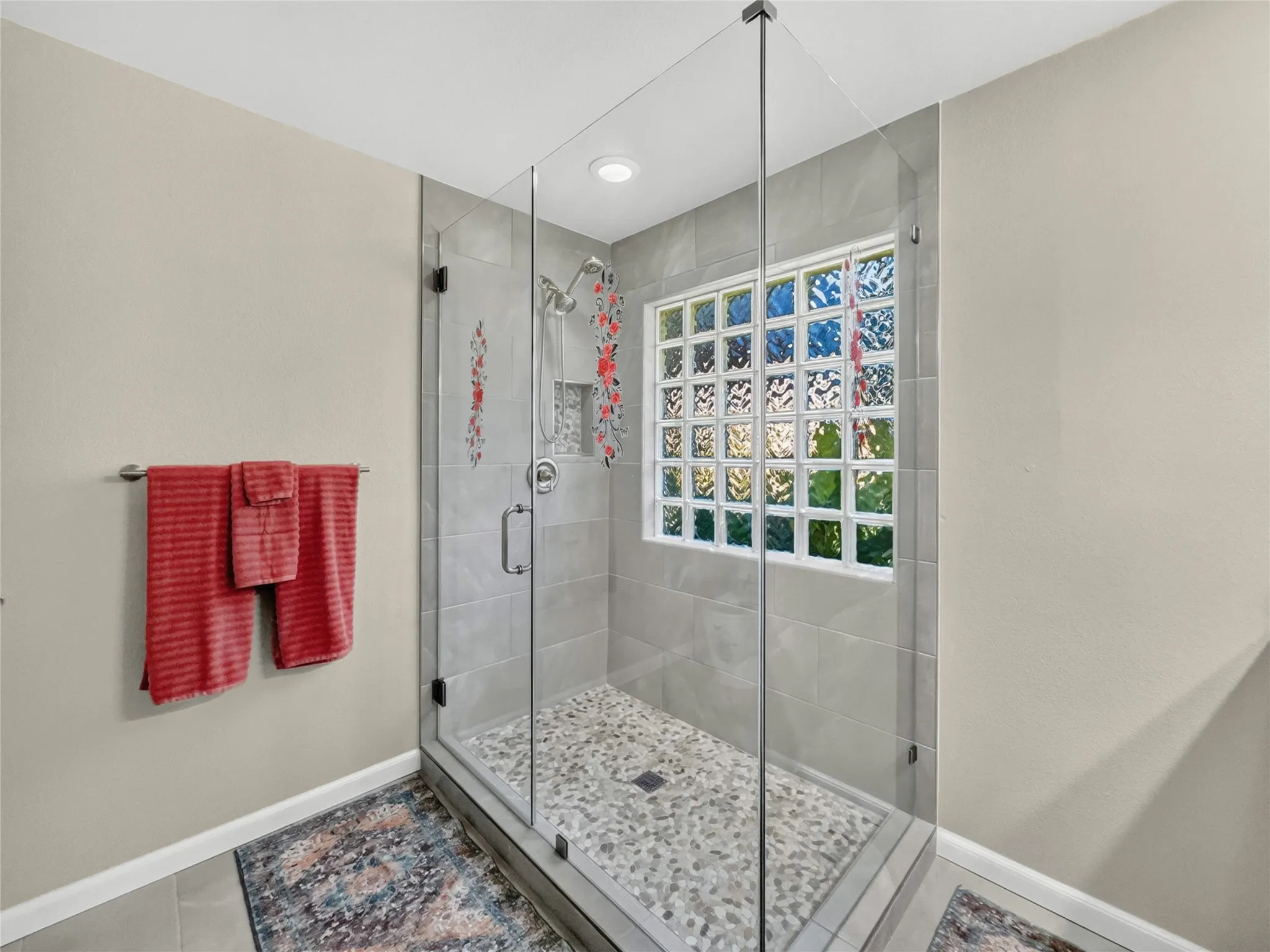 Glass-enclosed shower featuring a pebble floor, tiled walls, a built-in shower niche, and a glass block window