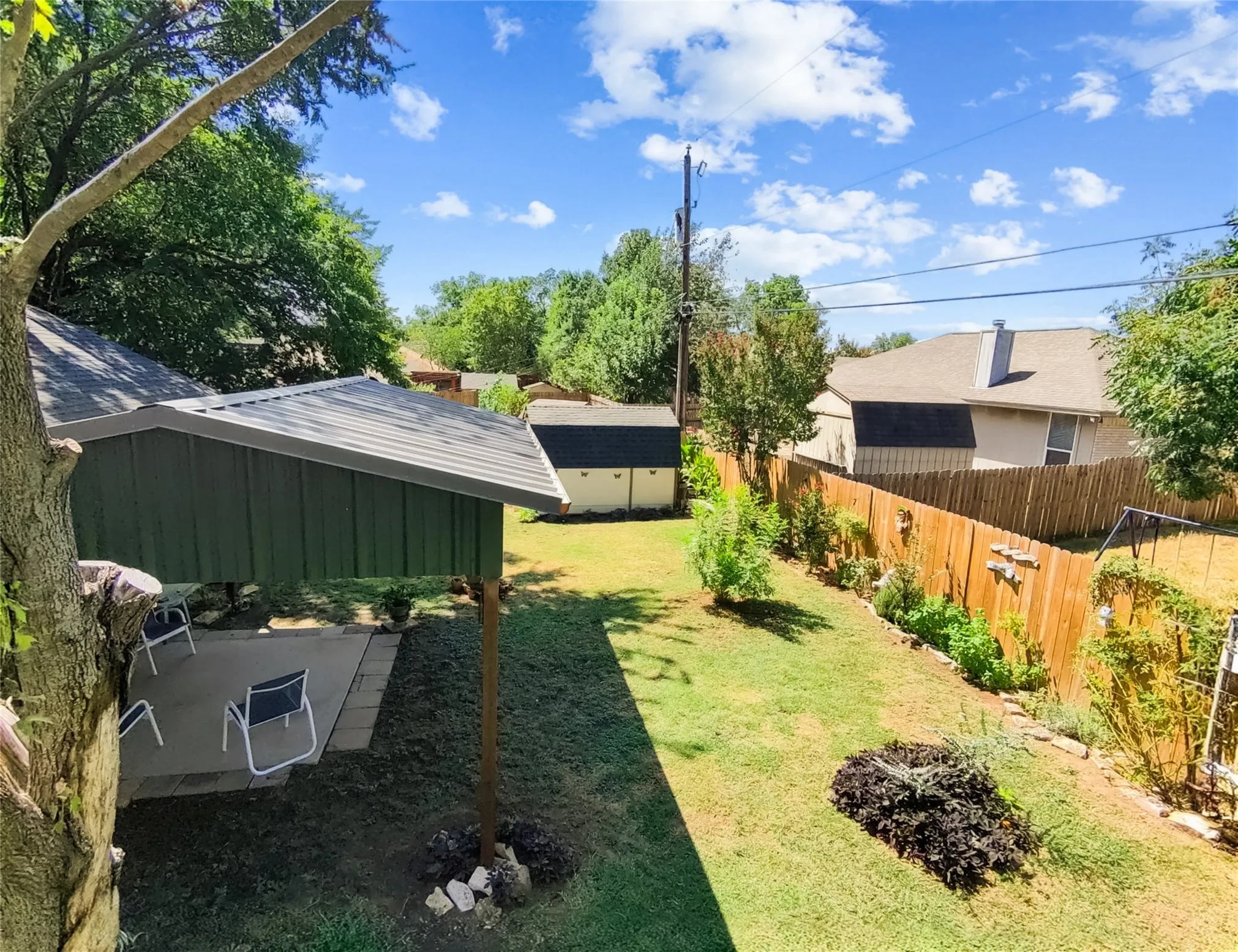 Expansive backyard featuring a covered patio, a storage shed, a wood privacy fence, a lush lawn, and mature trees