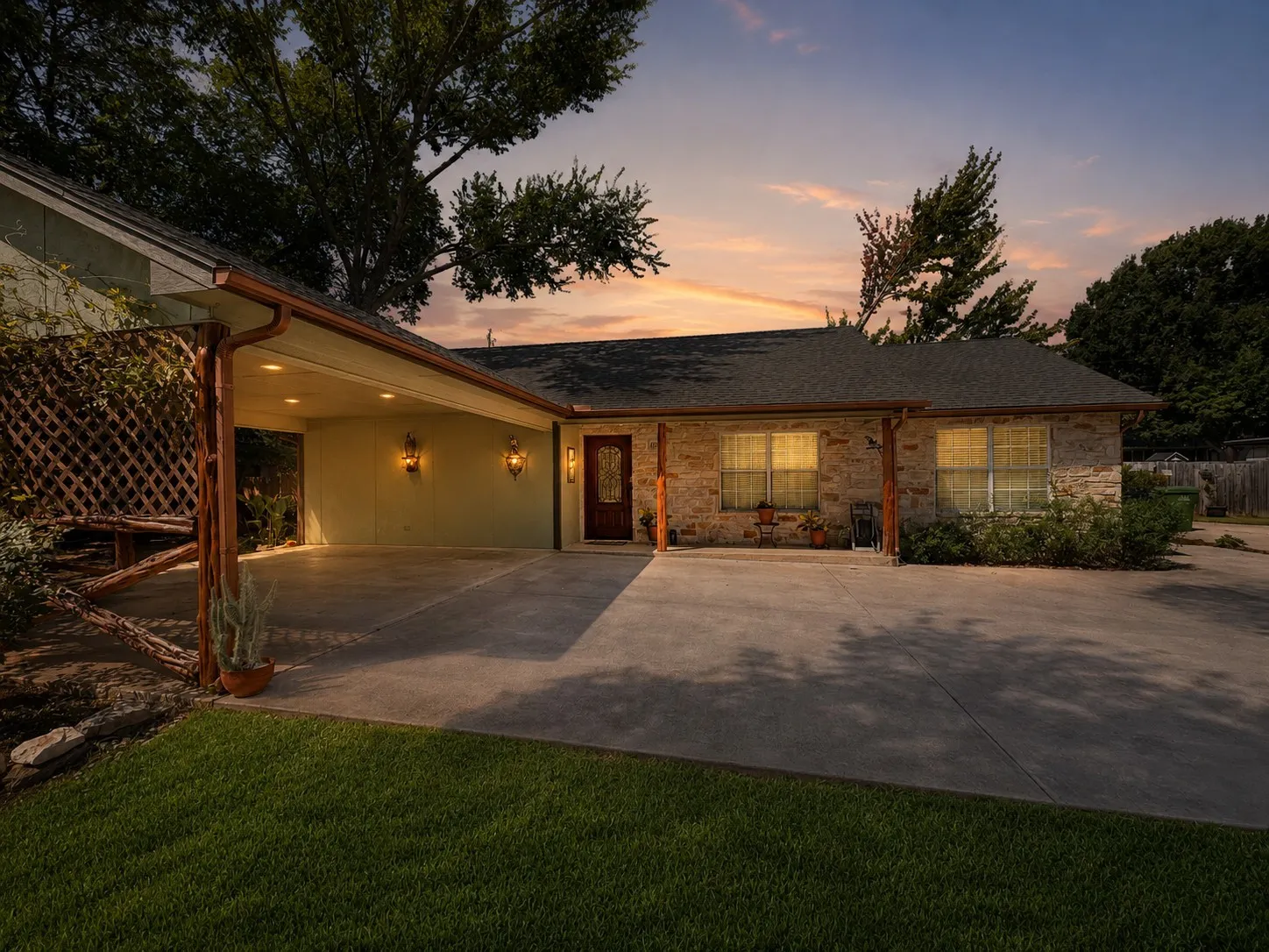Stone and stucco exterior with a covered carport, decorative lattice fencing, and a prominent front entry door