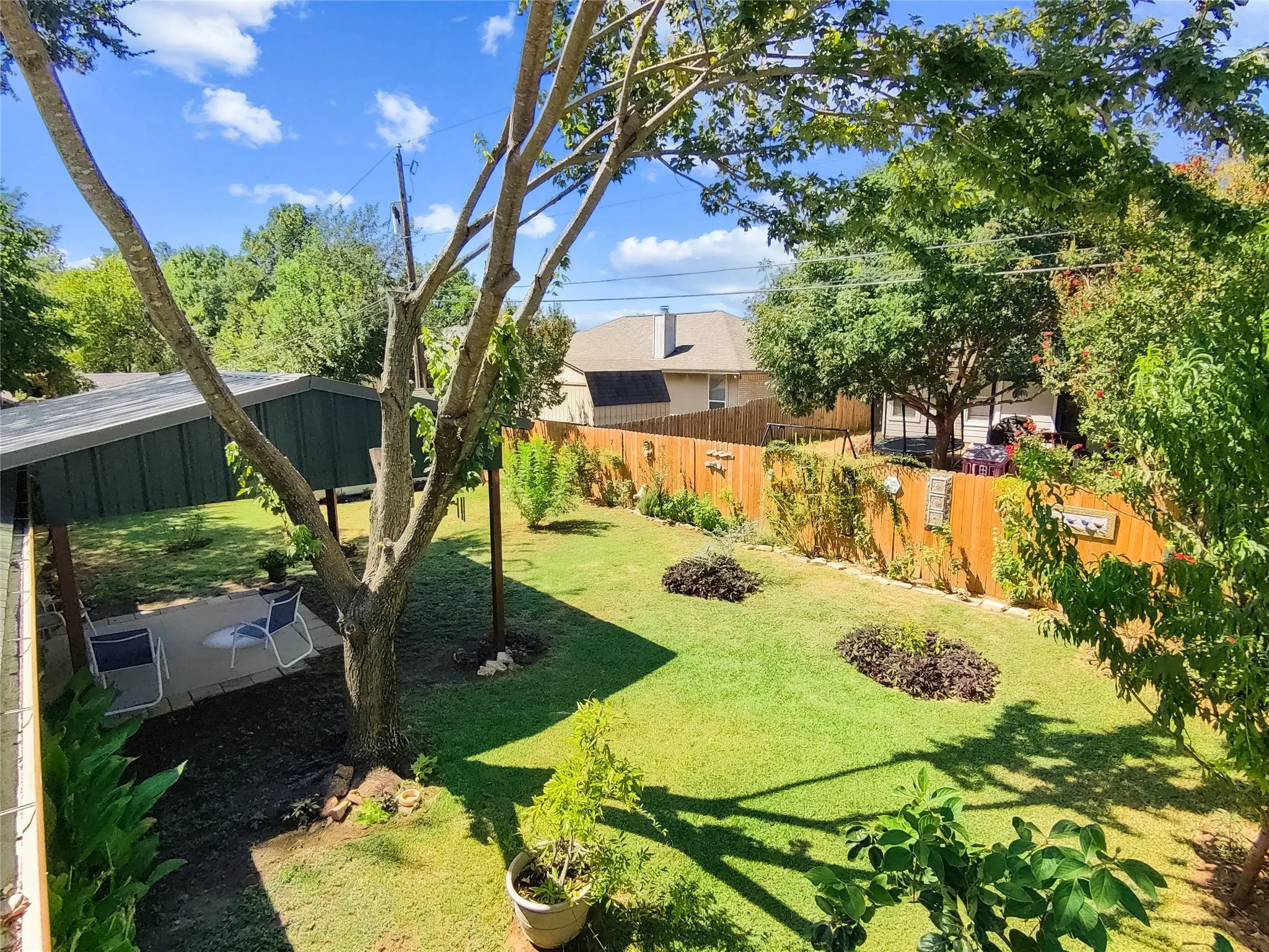 Expansive backyard featuring a manicured lawn, mature trees, a covered patio, and a wood privacy fence