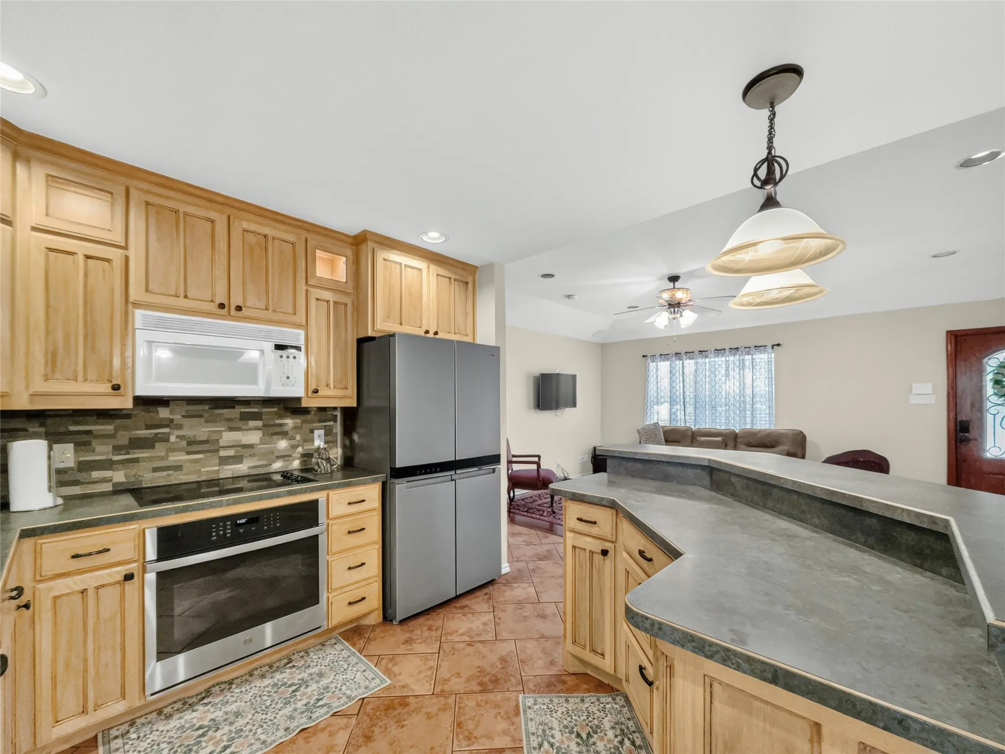 Kitchen featuring natural wood cabinetry, stone-finish countertops, stainless steel appliances, a tile backsplash, and ceramic tile flooring