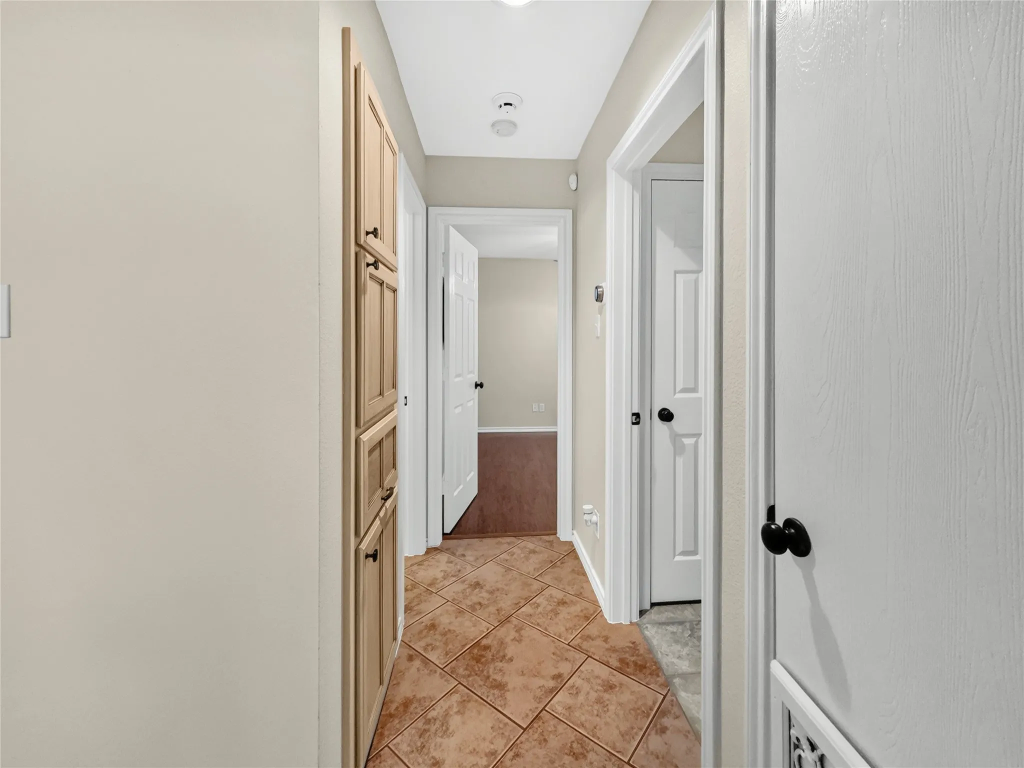 Hallway featuring tile flooring, built-in cabinetry with black hardware, and white interior doors