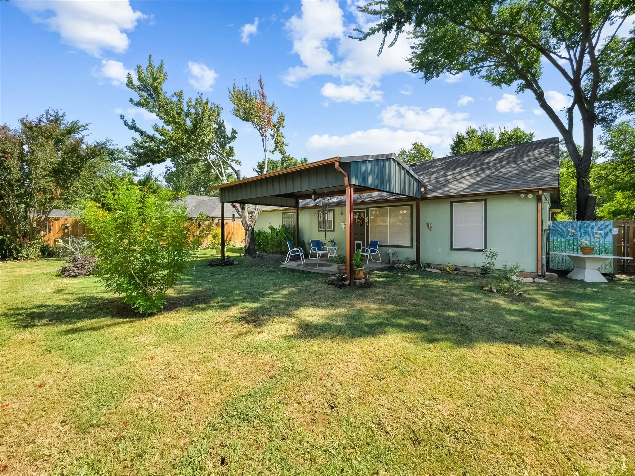 Expansive backyard featuring a covered patio, mature trees, and a privacy fence