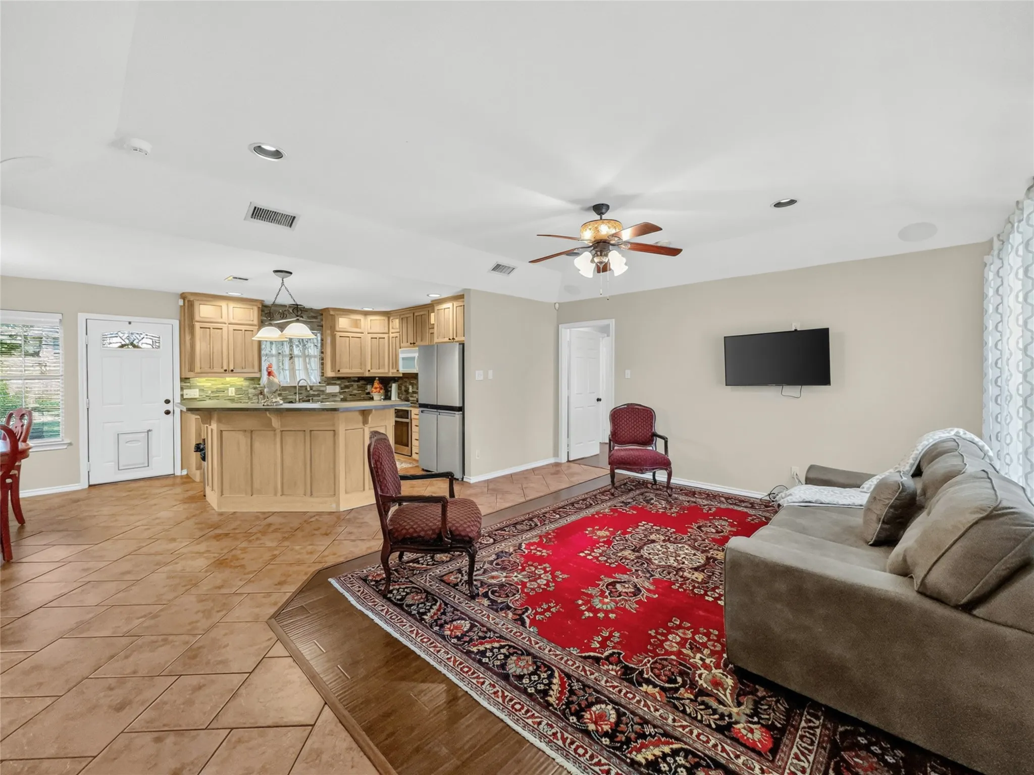 Open-concept living area with tile flooring, recessed lighting, ceiling fan, and a kitchen featuring wood cabinetry, stainless steel appliances, and a breakfast bar with pendant lighting