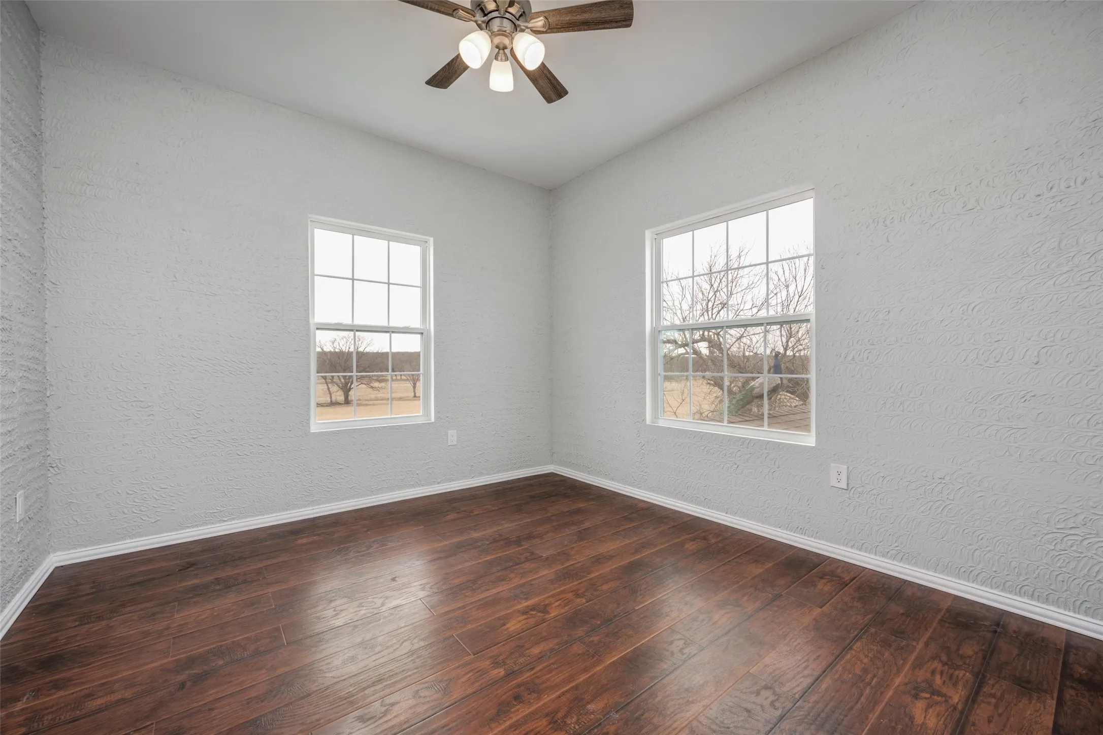 Wood-finish flooring, white trim, textured walls, and a ceiling fan with integrated lighting