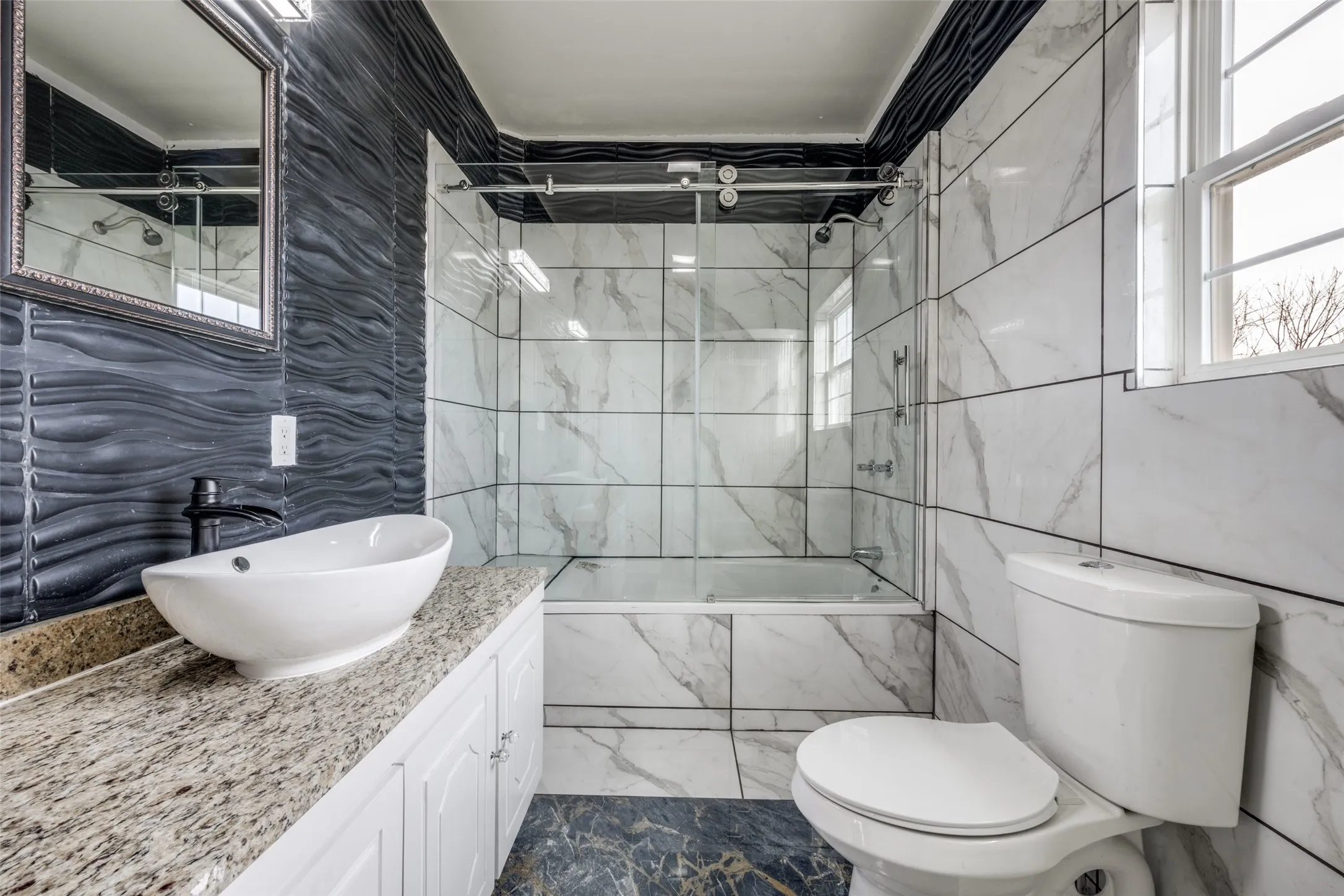 Bathroom featuring a vessel sink, granite countertop, white cabinetry, a tiled shower-tub combination with glass enclosure, and a window
