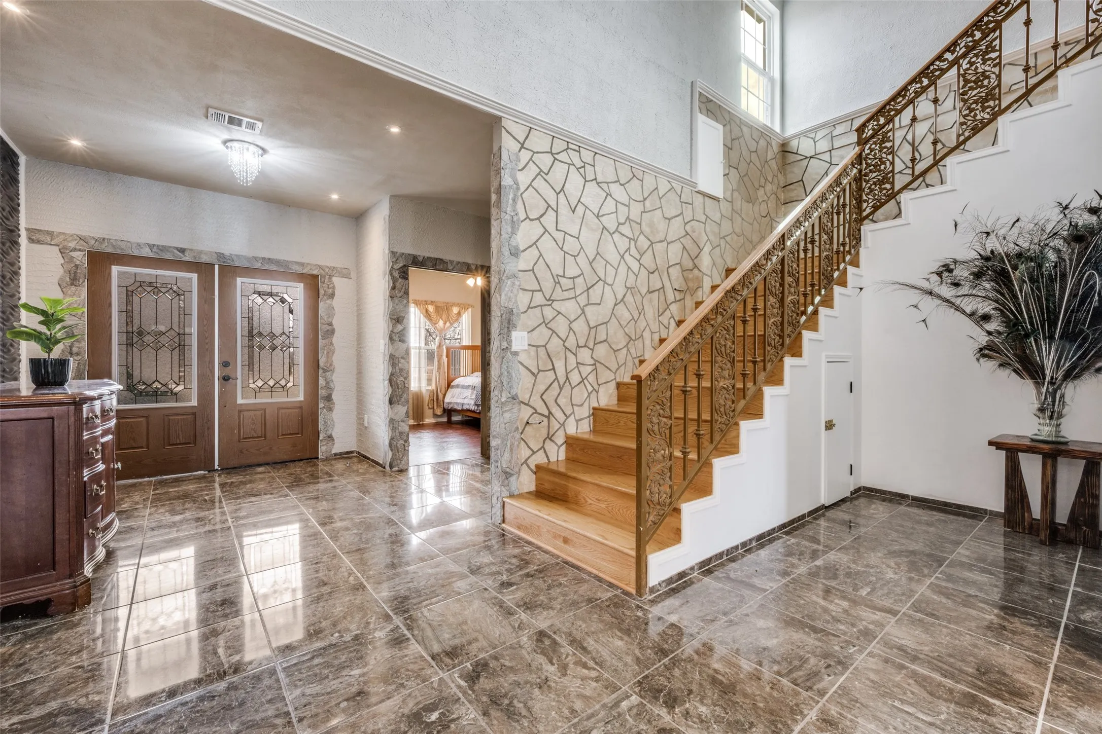 Entryway featuring stone-look wall accents, double entry doors with decorative glass panels, a grand staircase with an ornate metal railing and wood treads, and polished tile flooring