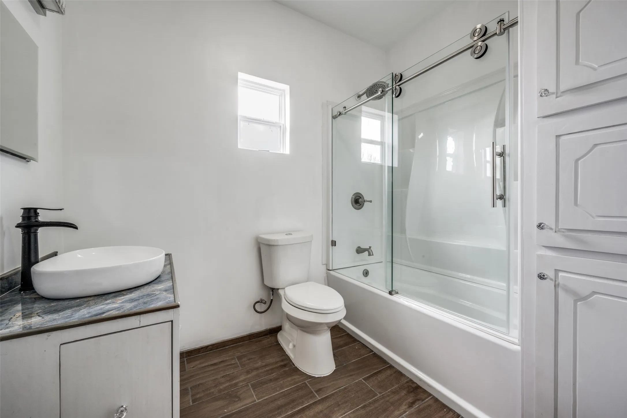 Wood-finish flooring with a vessel sink vanity, matte black faucet, and built-in storage cabinetry