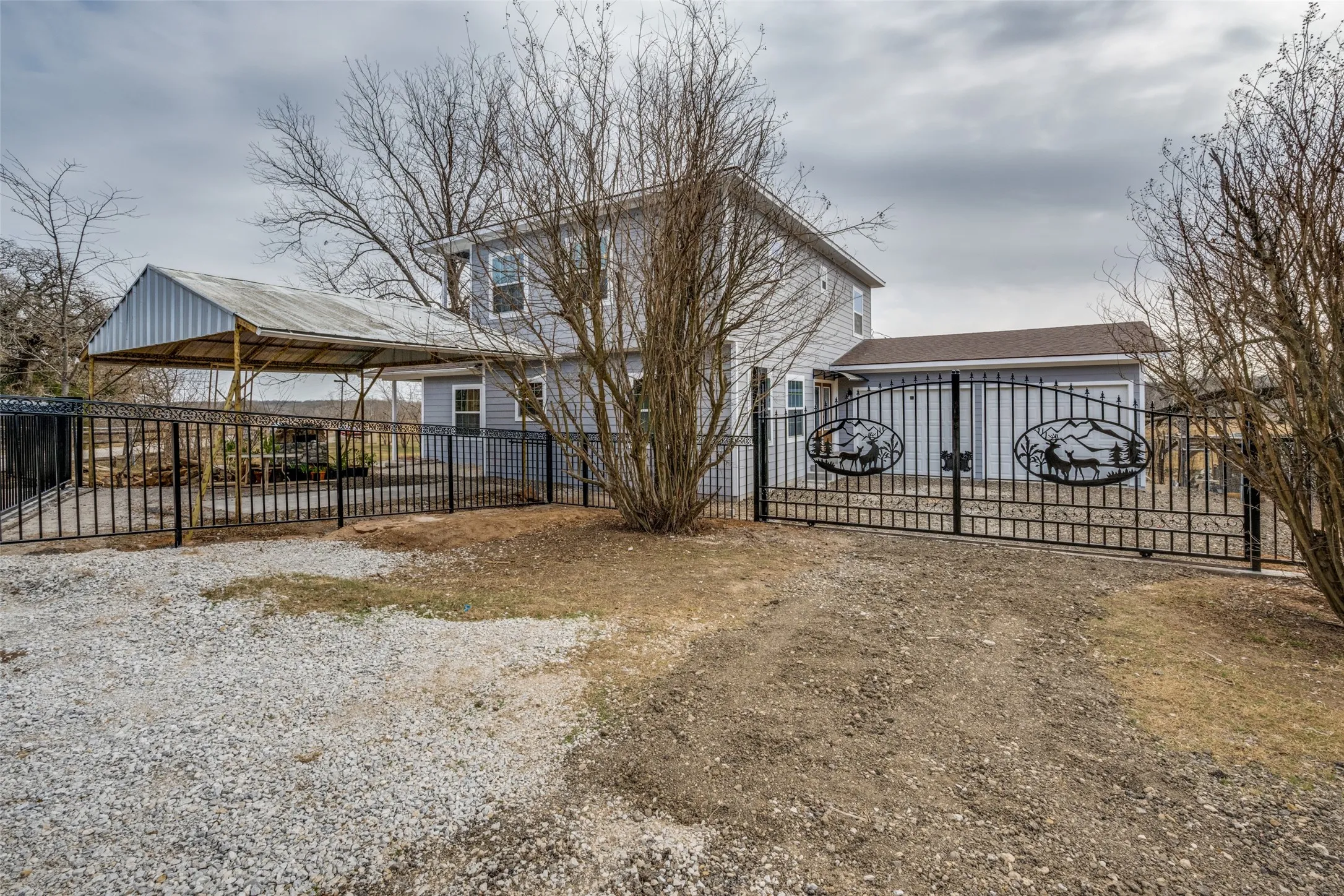 Gated property entrance with decorative metalwork, a detached carport, and a separate garage structure