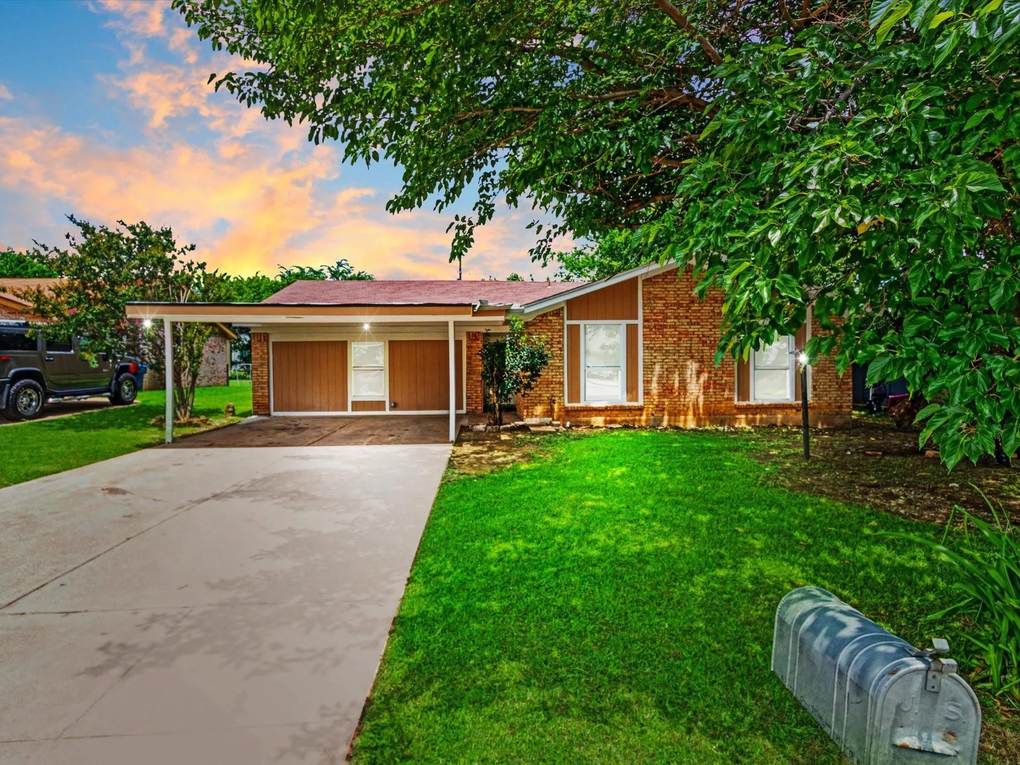 Brick exterior with vertical wood paneling, featuring a covered carport, concrete driveway, and established front landscaping