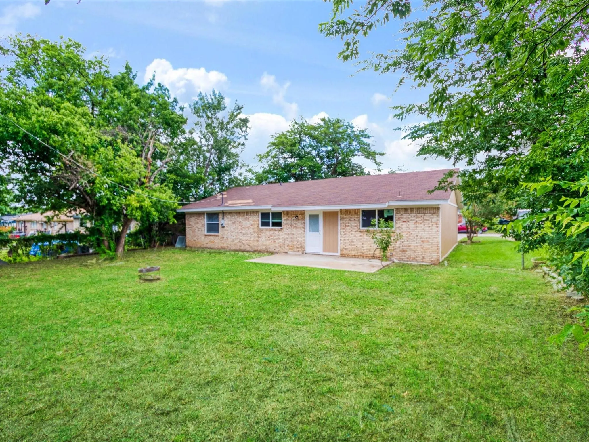 Expansive rear lawn featuring a concrete patio, brick exterior, and mature trees