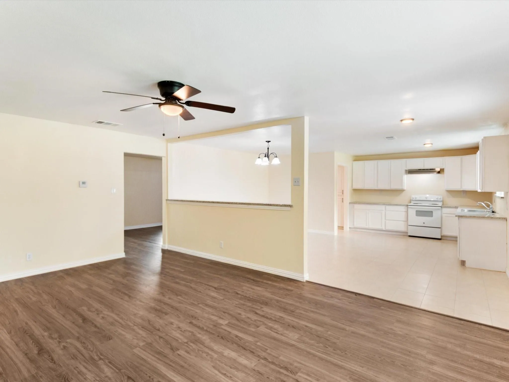 Wood-finish flooring, ceiling fan with integrated lighting, white kitchen cabinetry, white kitchen appliances, and tile flooring in the kitchen
